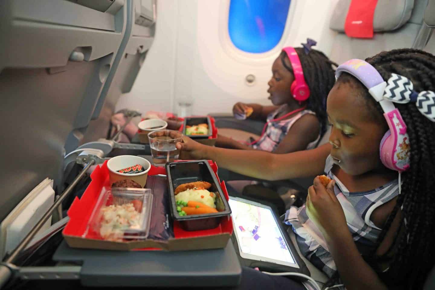 Two girls watching tablets while eating airplane food