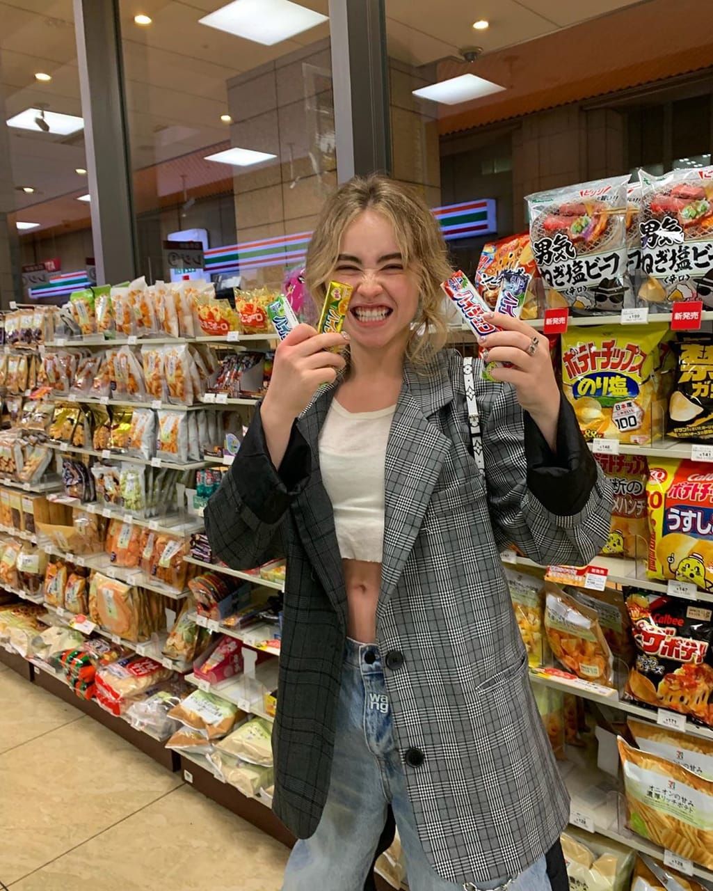 Sabrina Carpenter in a convenience store in Tokyo Japan holding up candy bars