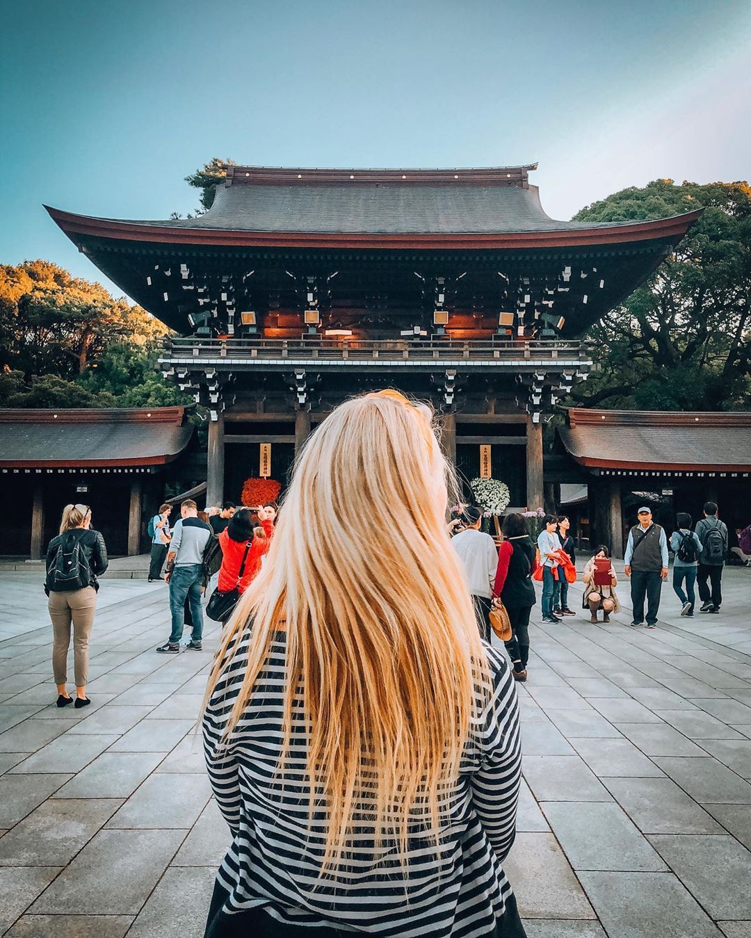 Blonde woman in foreground with her back to the camera and Meiji Shrine in the background
