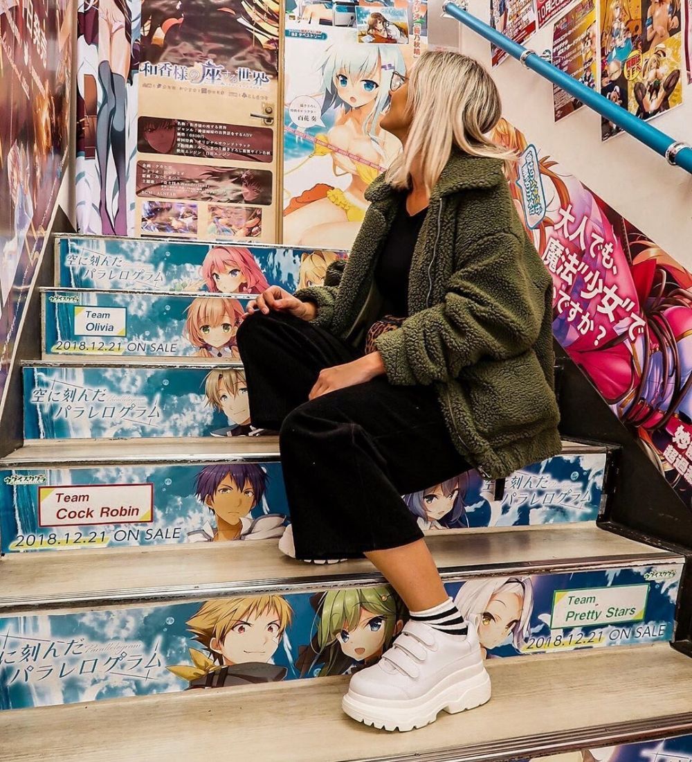 Woman sitting on steps covered with anime art in Akihabara Tokyo Japan