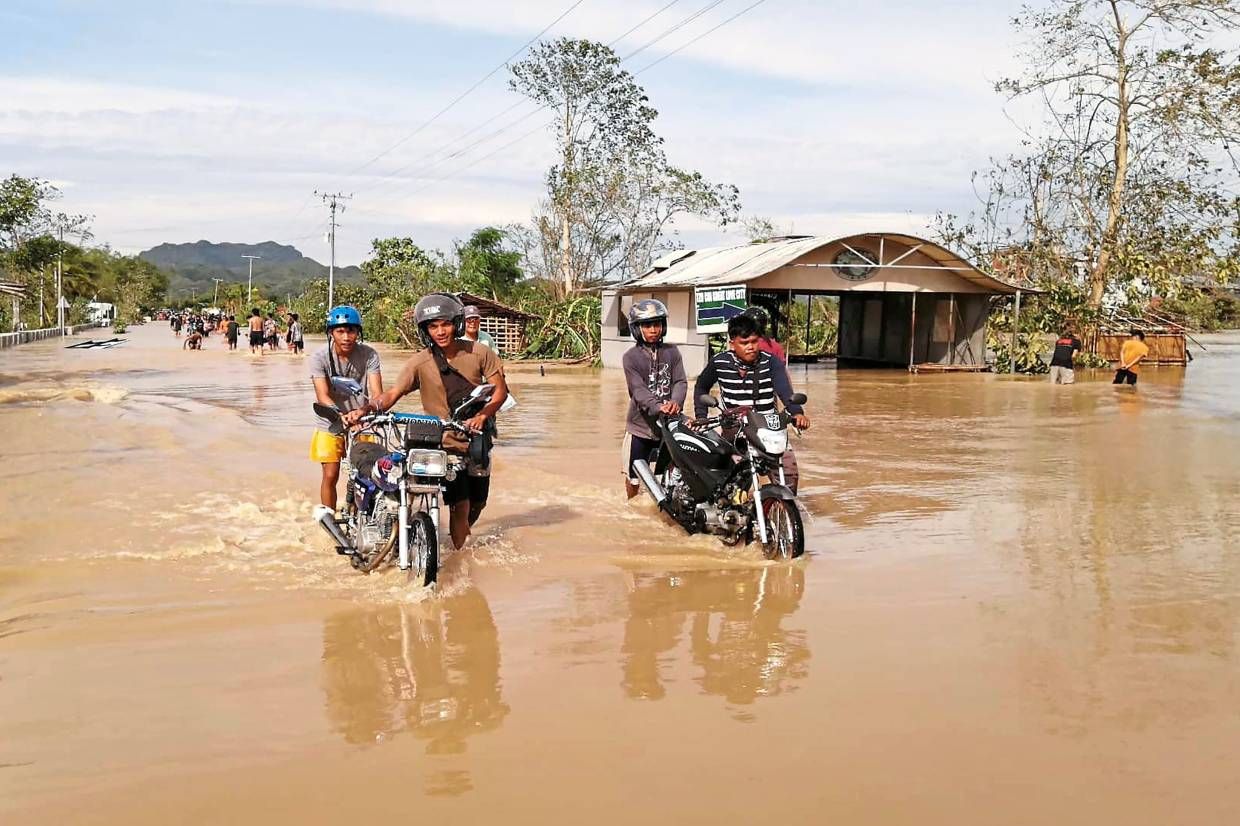 People pushing motorcycles through floodwater in the Philippines
