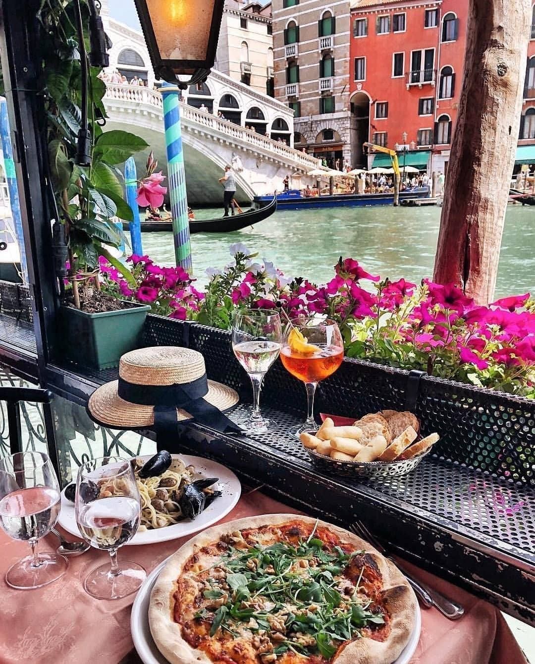 Plates of food and glasses of wine on table next to Venice canal in Italy