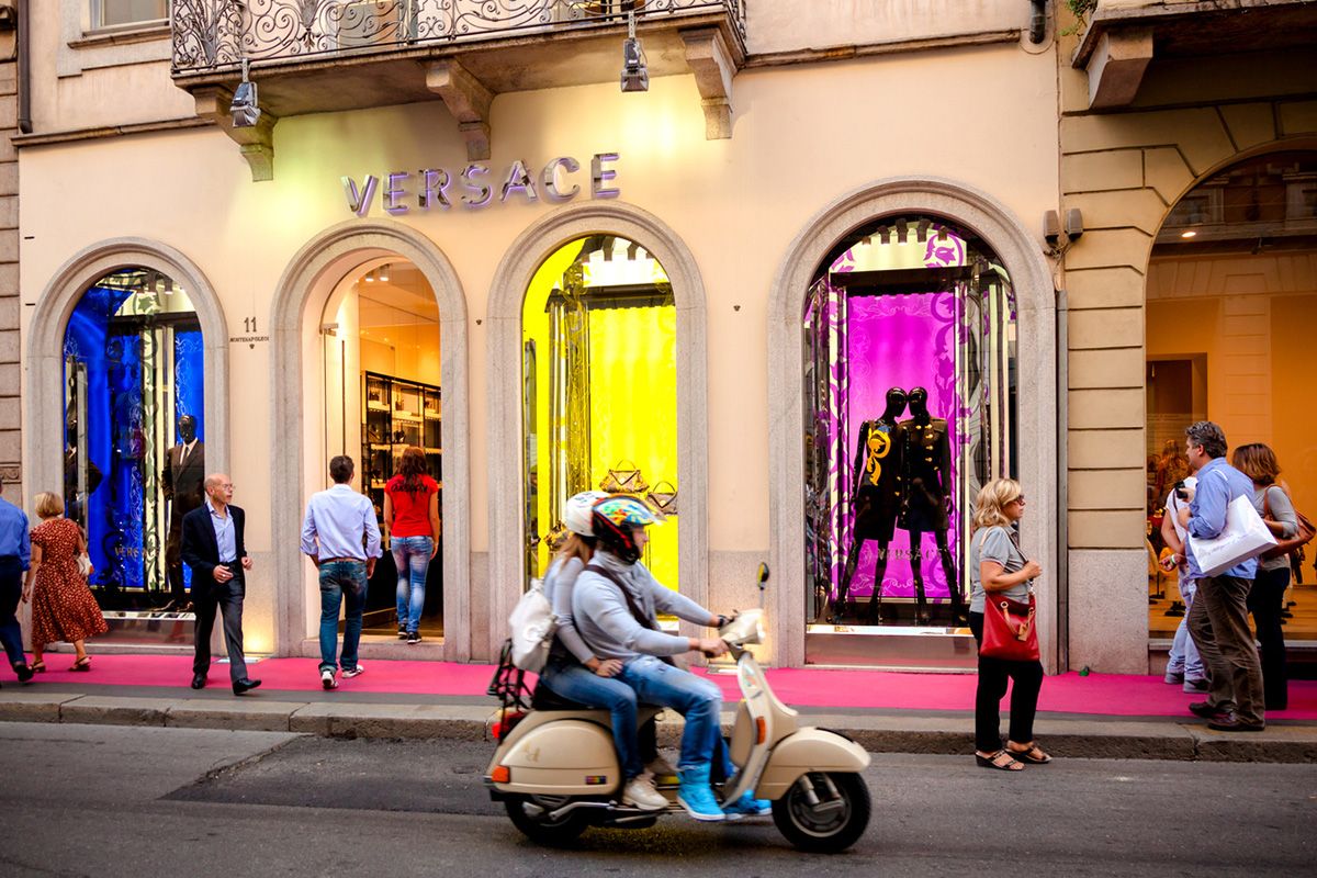 Two people on a vespa riding past a Versace store in Italy