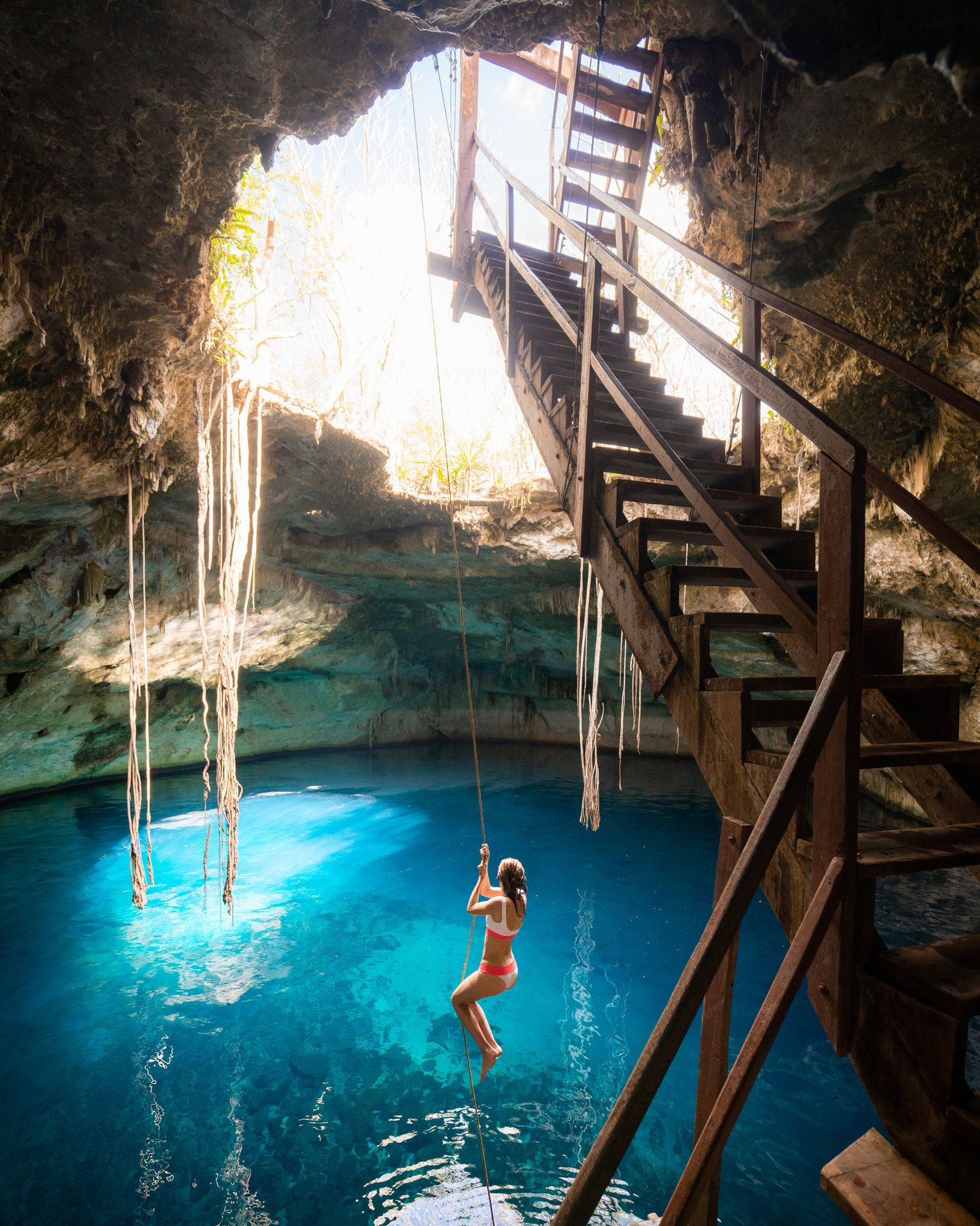 Woman swinging from rope inside cenote in Mexico