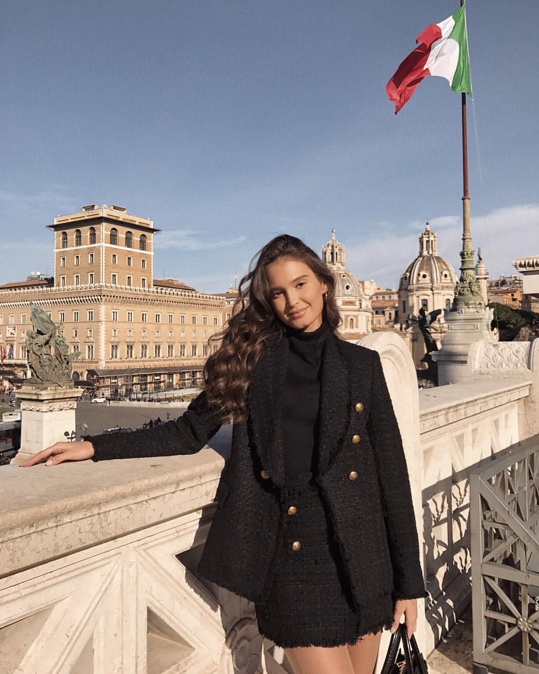 Woman in winter coat standing by cement railing with Italian flag in background