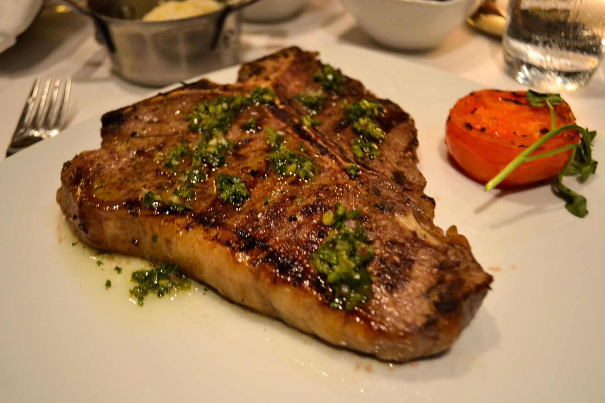 a steak and grilled tomato with green herbs