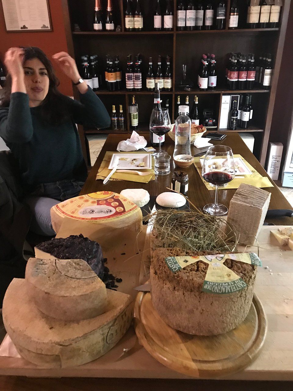 Woman drinking wine next to cheese wheels