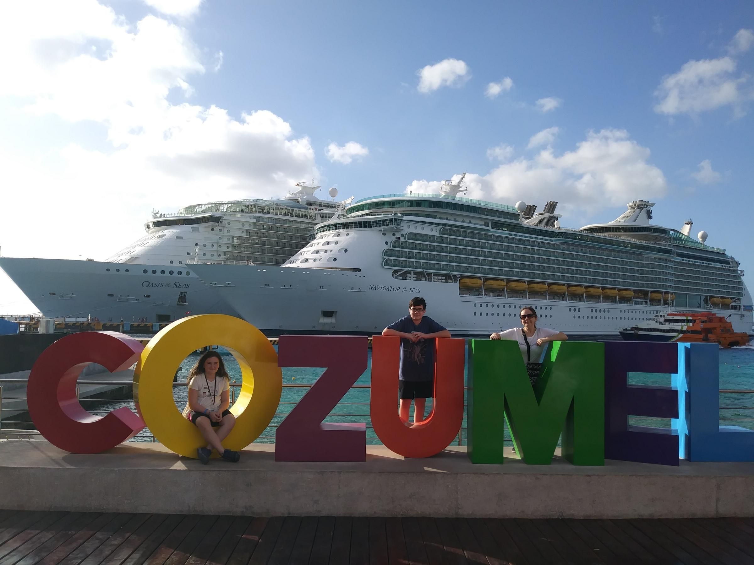 Three people posing with Cozumel sign with cruise ship in background