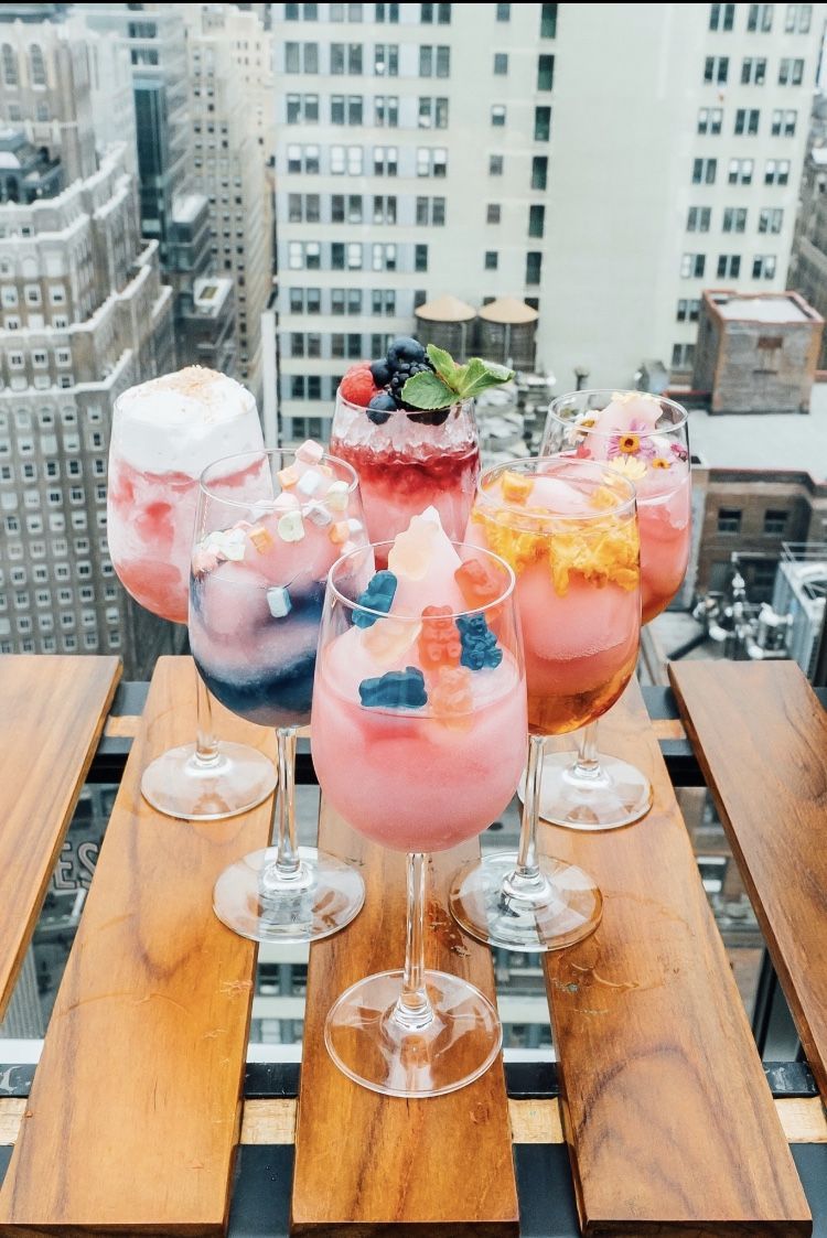 six glasses of frozen rose topped with fruit and gummy bears overlooking nyc skyscrapers