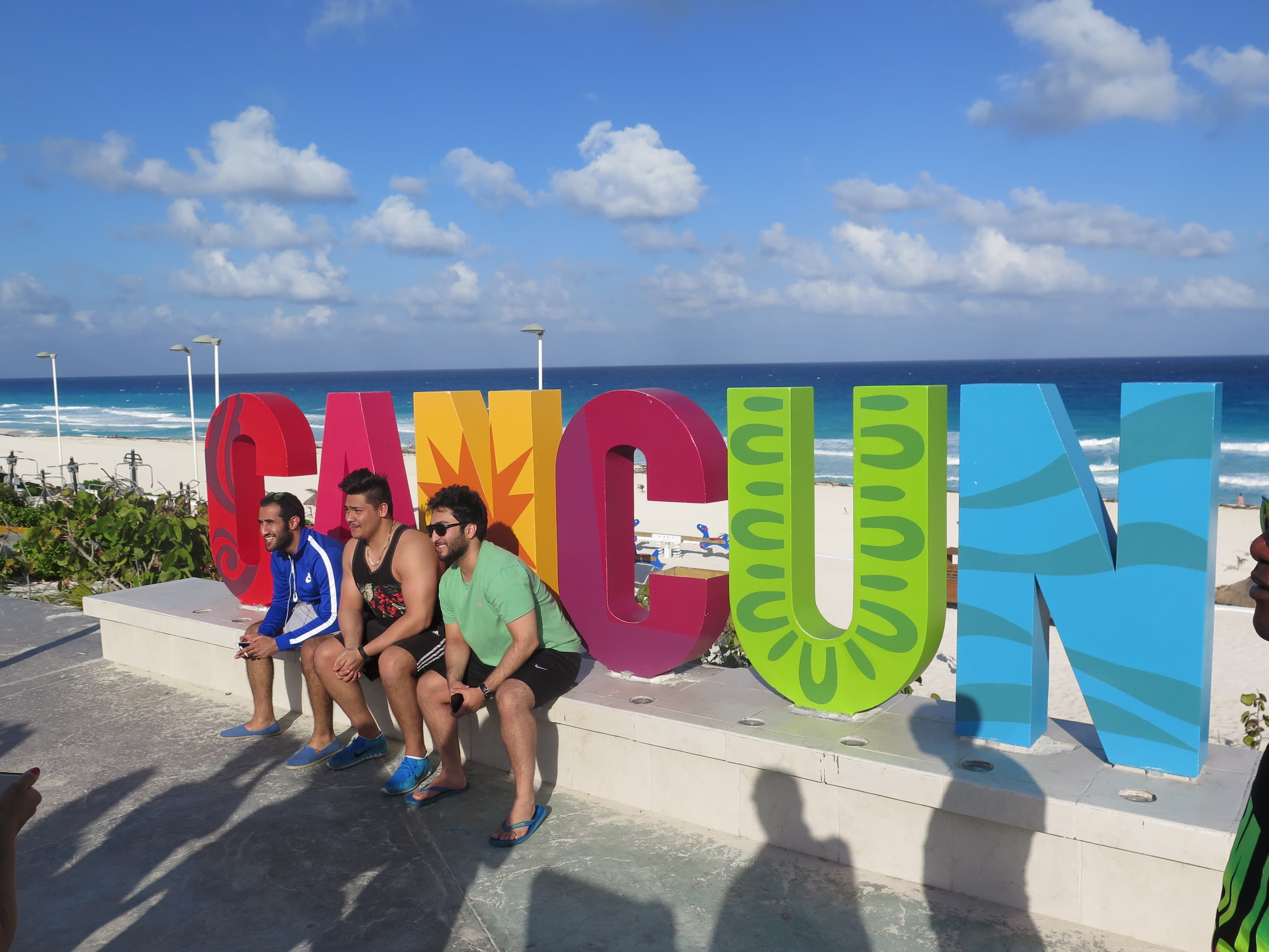 guys taking photos by cancun sign