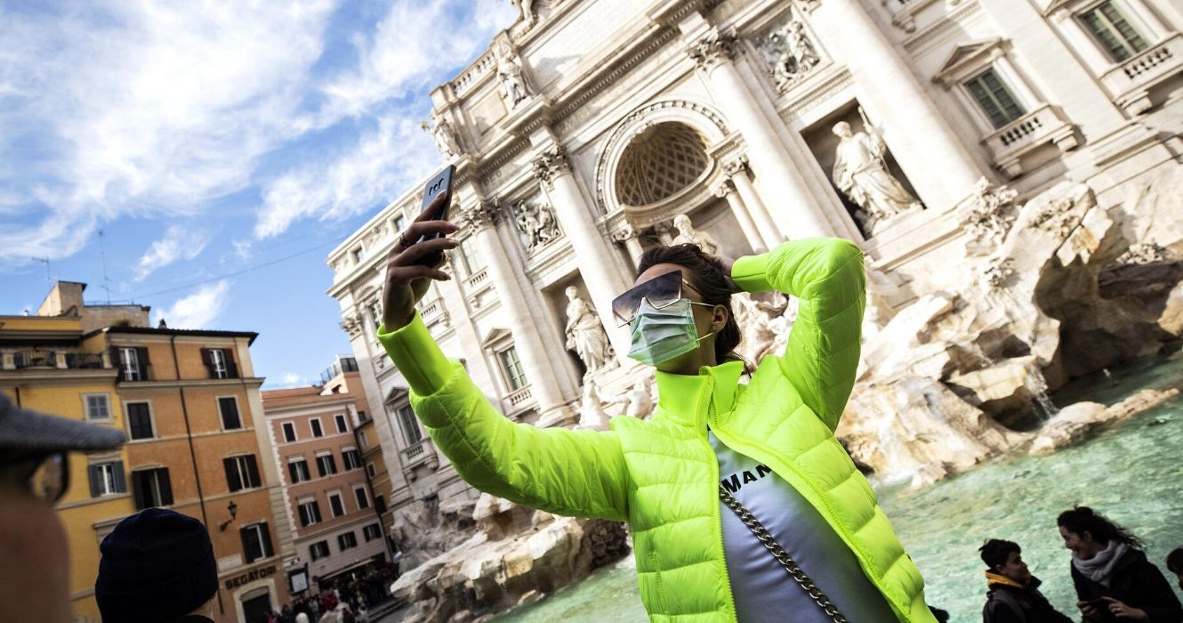 Tourist wearing a face mask taking a selfie in front of the Trevi Fountain