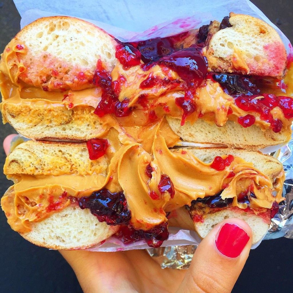 hand holding up peanut butter and jelly bagel red fingernail