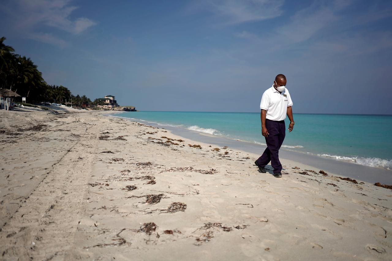a man in a face mask walks along a beach in jamaica