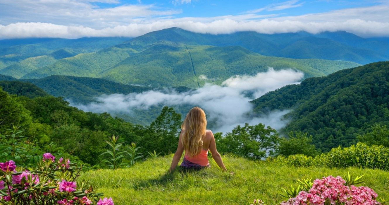 A woman sitting on top of mountains in the Blue Ridge Mountains, North Carolina, USA