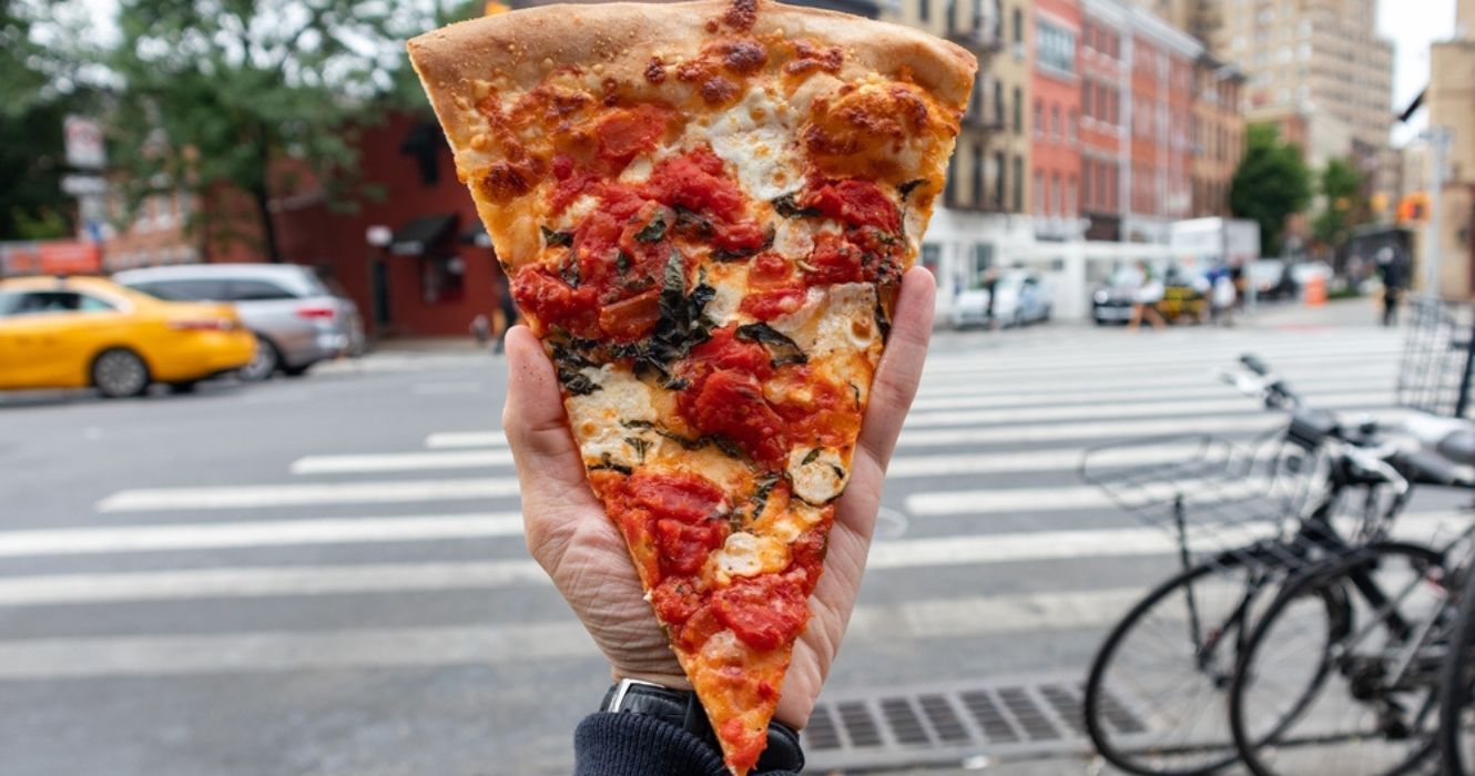 Hand holding a pizza slice in New York City