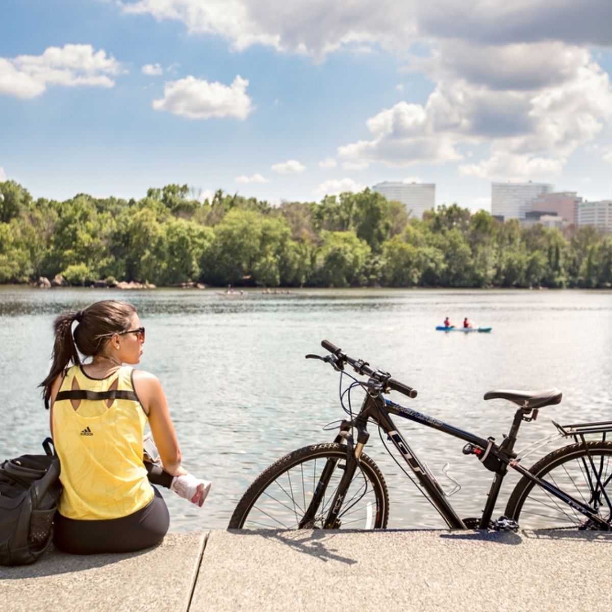 A girl sitting in front of river with bicycle parked on side