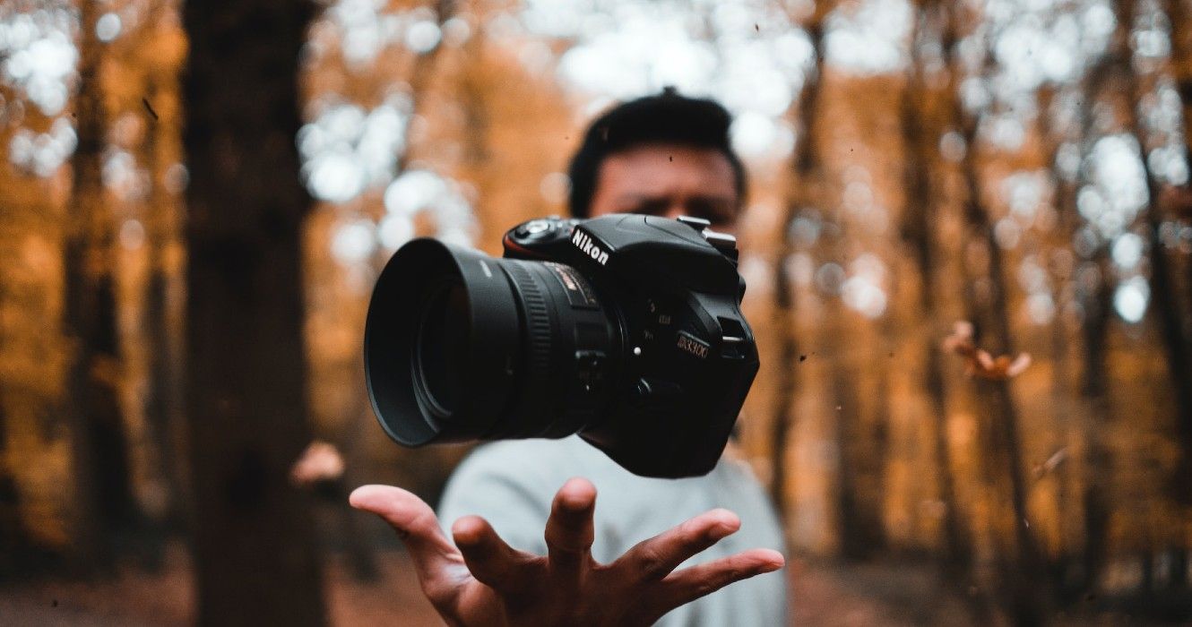 Snapshot of a person with a camera just above their hand with trees in the background 