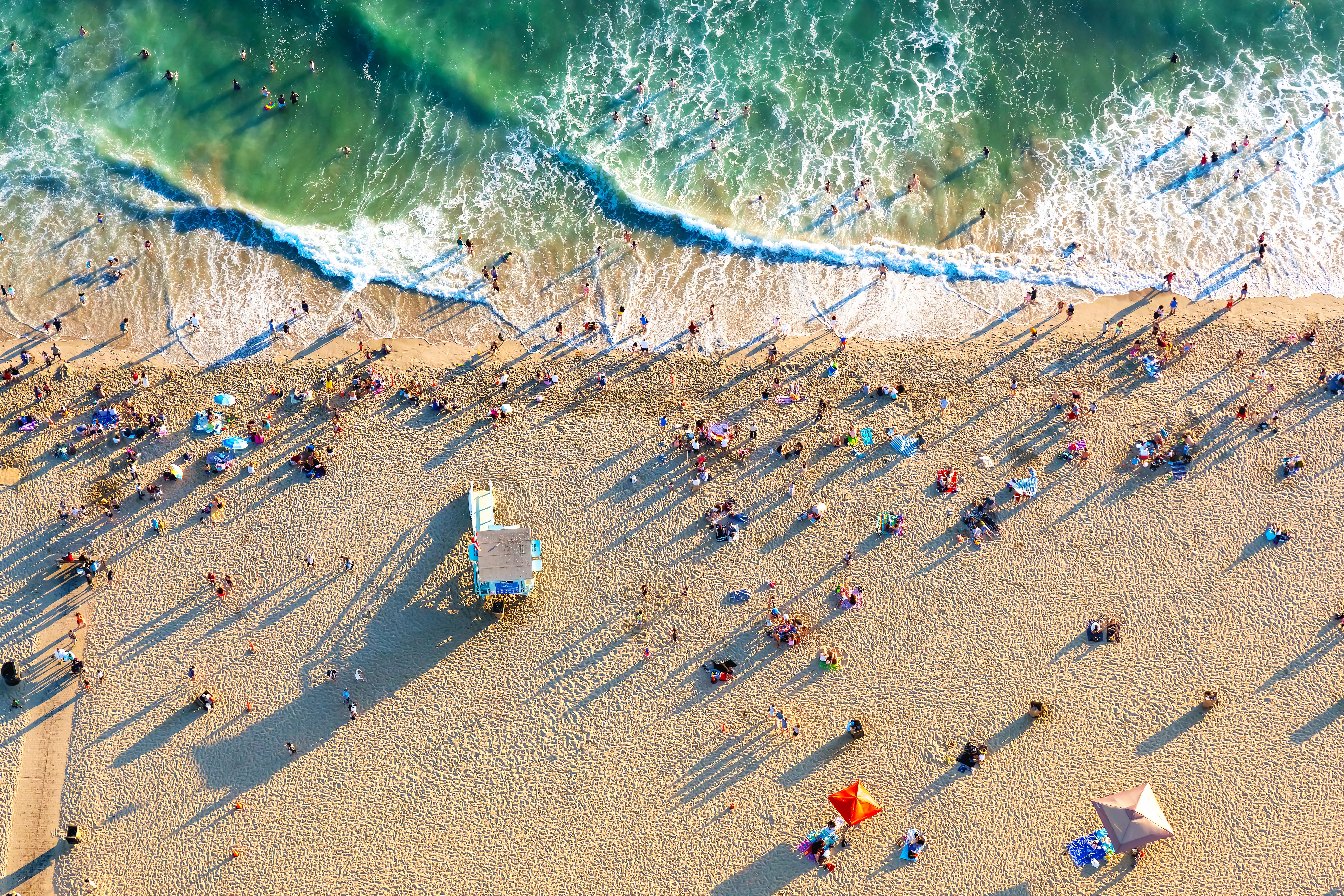 A birdseye view of Santa Monica Beach in LA with pedestrians, sunbathers, and swimmers on the sands