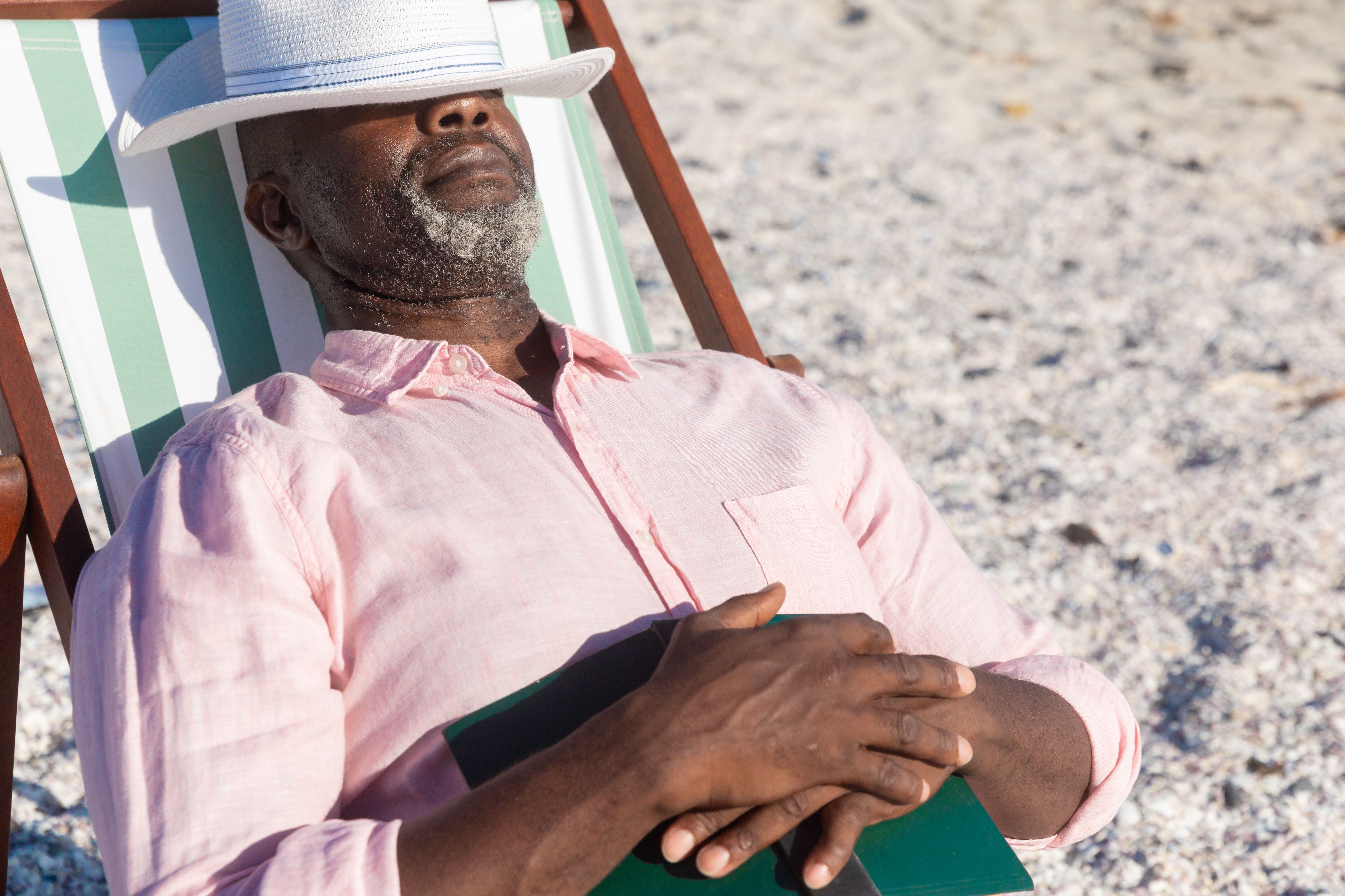man with hat over eyes sleeping on beach chair