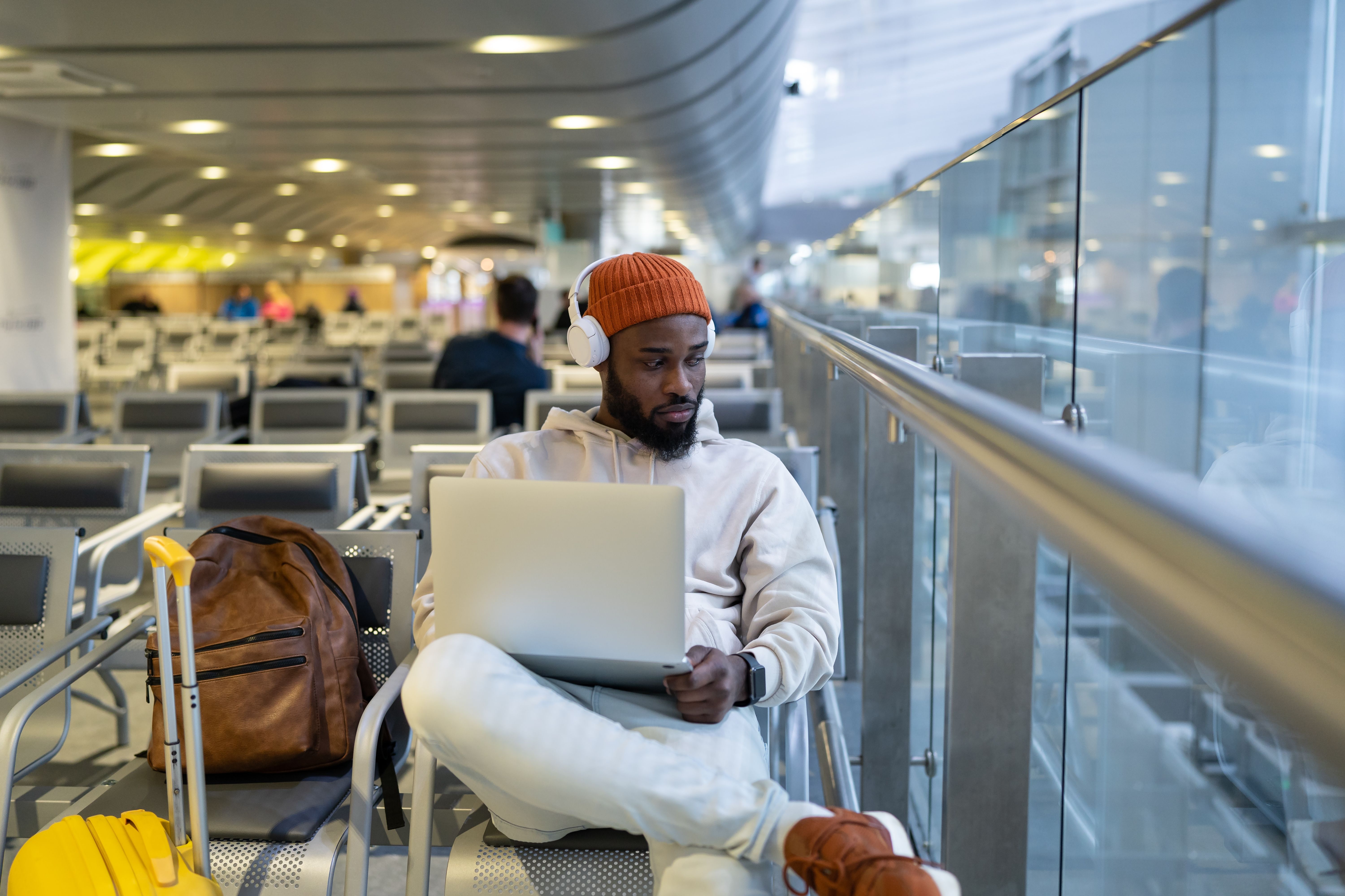 man listening to music on headphones with laptop in airport