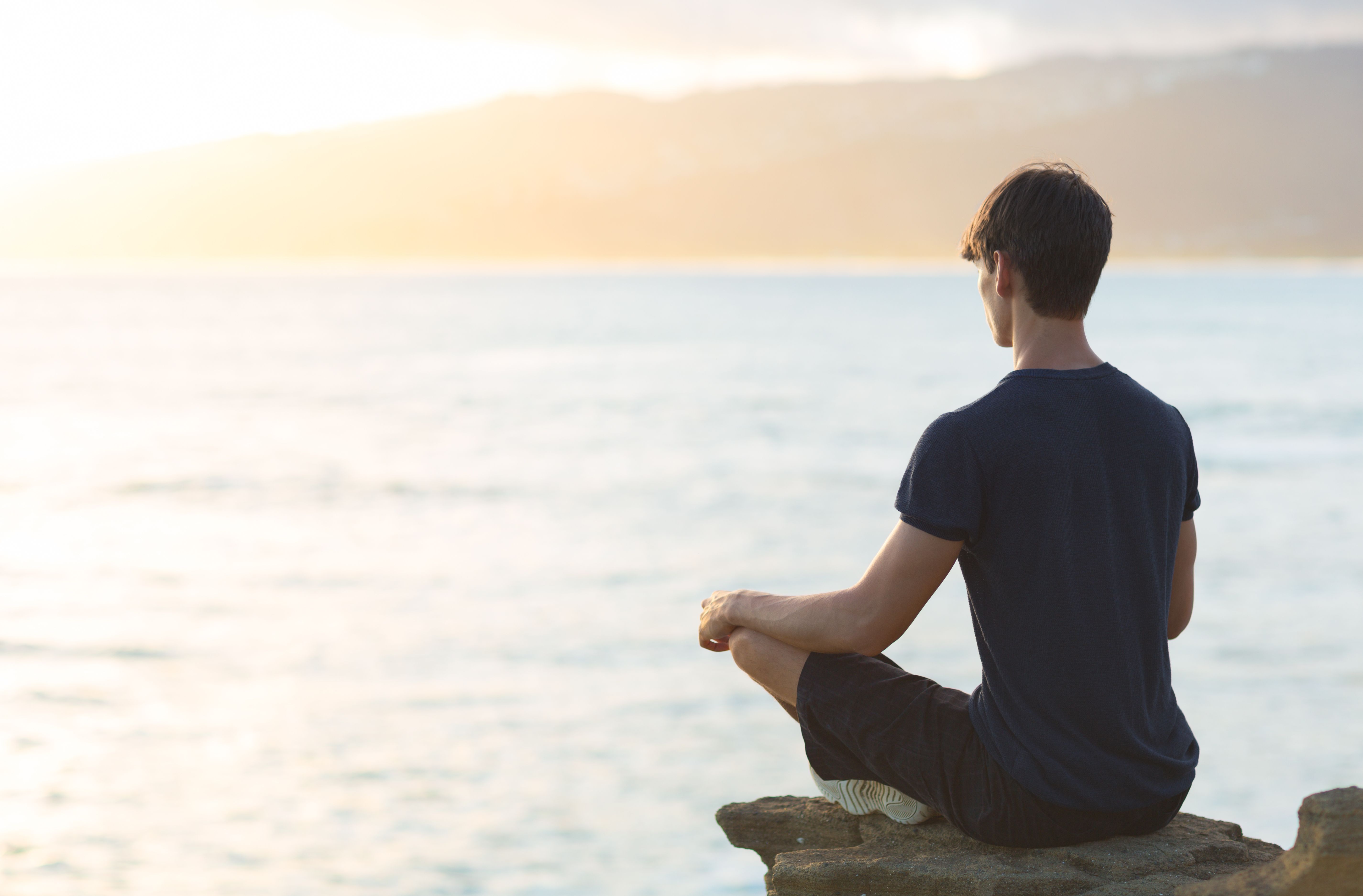 man sitting on rock meditating overlooking water