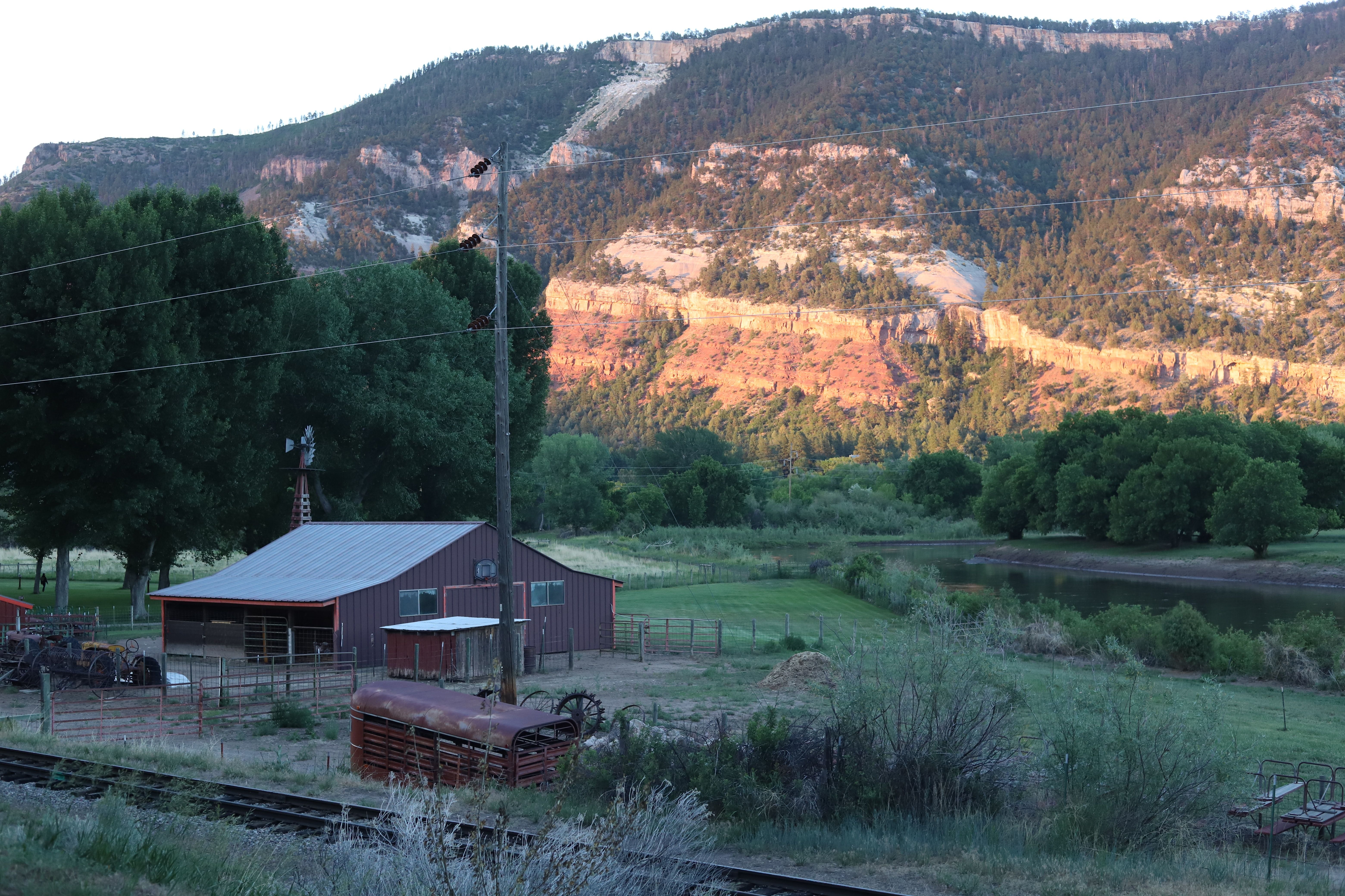 A wooden house located near a lush grass field and a mountain