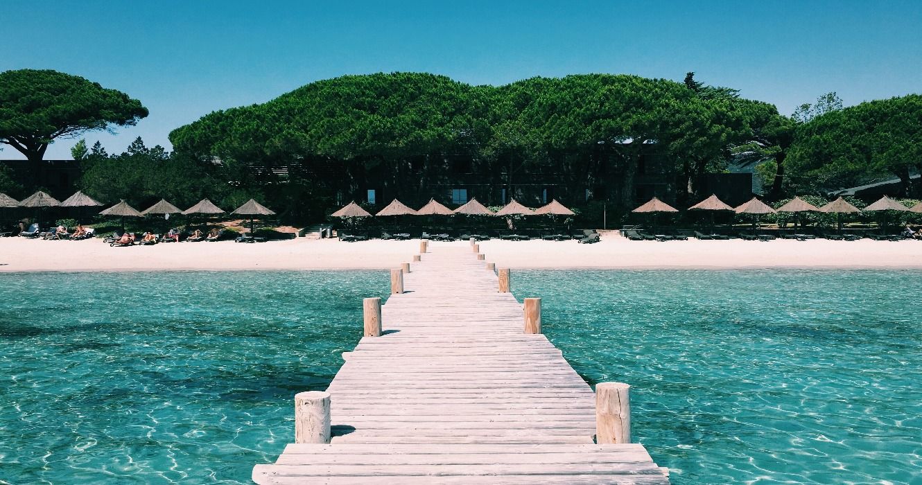 A boardwalk on the white-sand Palombaggia beach in Corsica, France, surrounded by crystal-clear blue waters