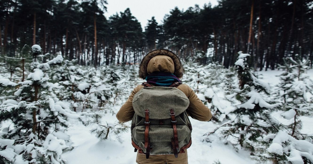 A backpacker hiking in the winter through a snow-covered forest