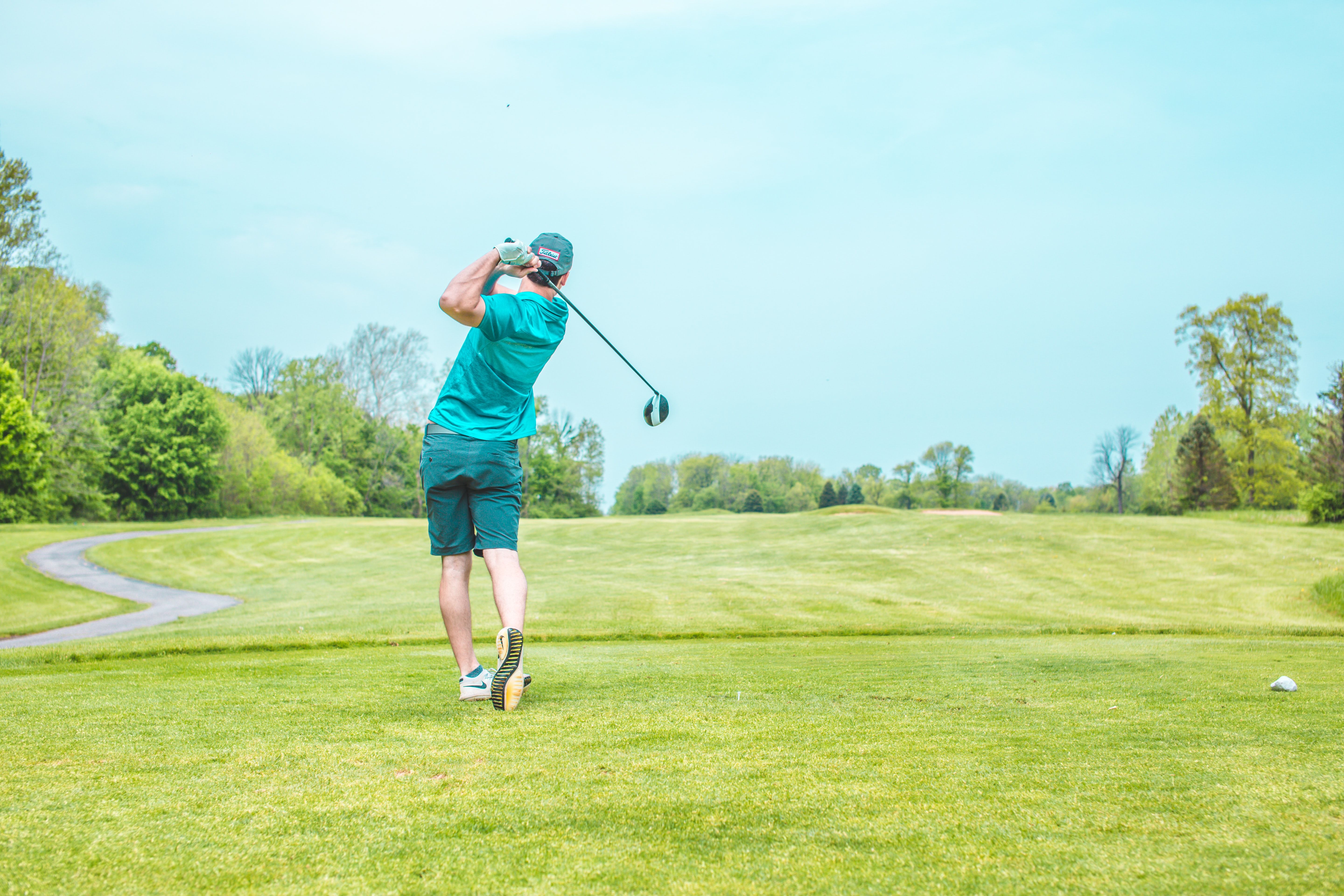 Man wearing blue shorts and a blue t-shirt playing golf in warm weather. 