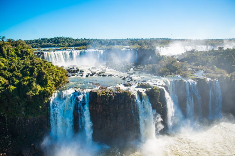 Iguazu Falls surrounded by trees under a blue sky