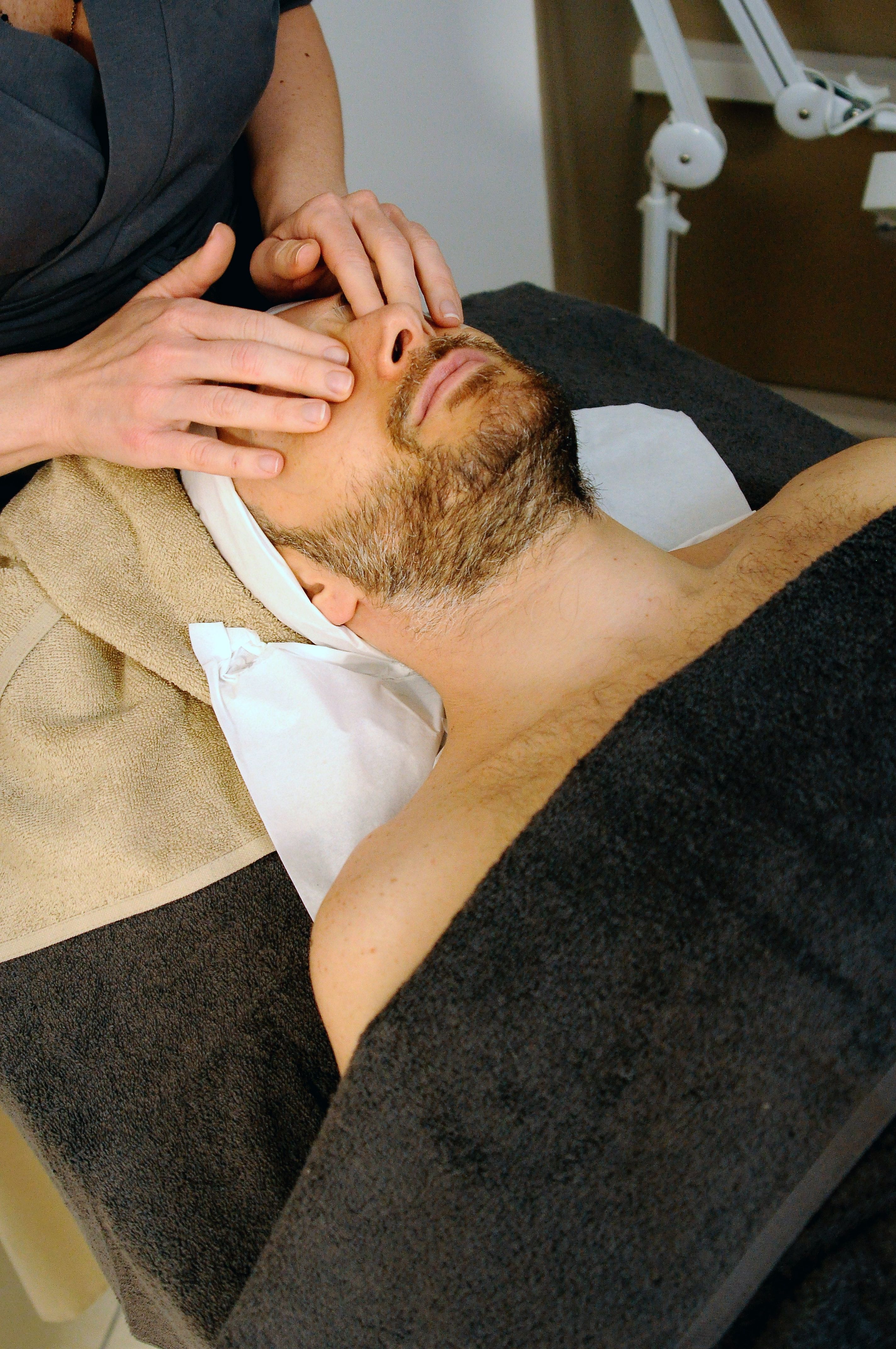 Homem recebe tratamento facial com os olhos fechados vestindo um roupão 