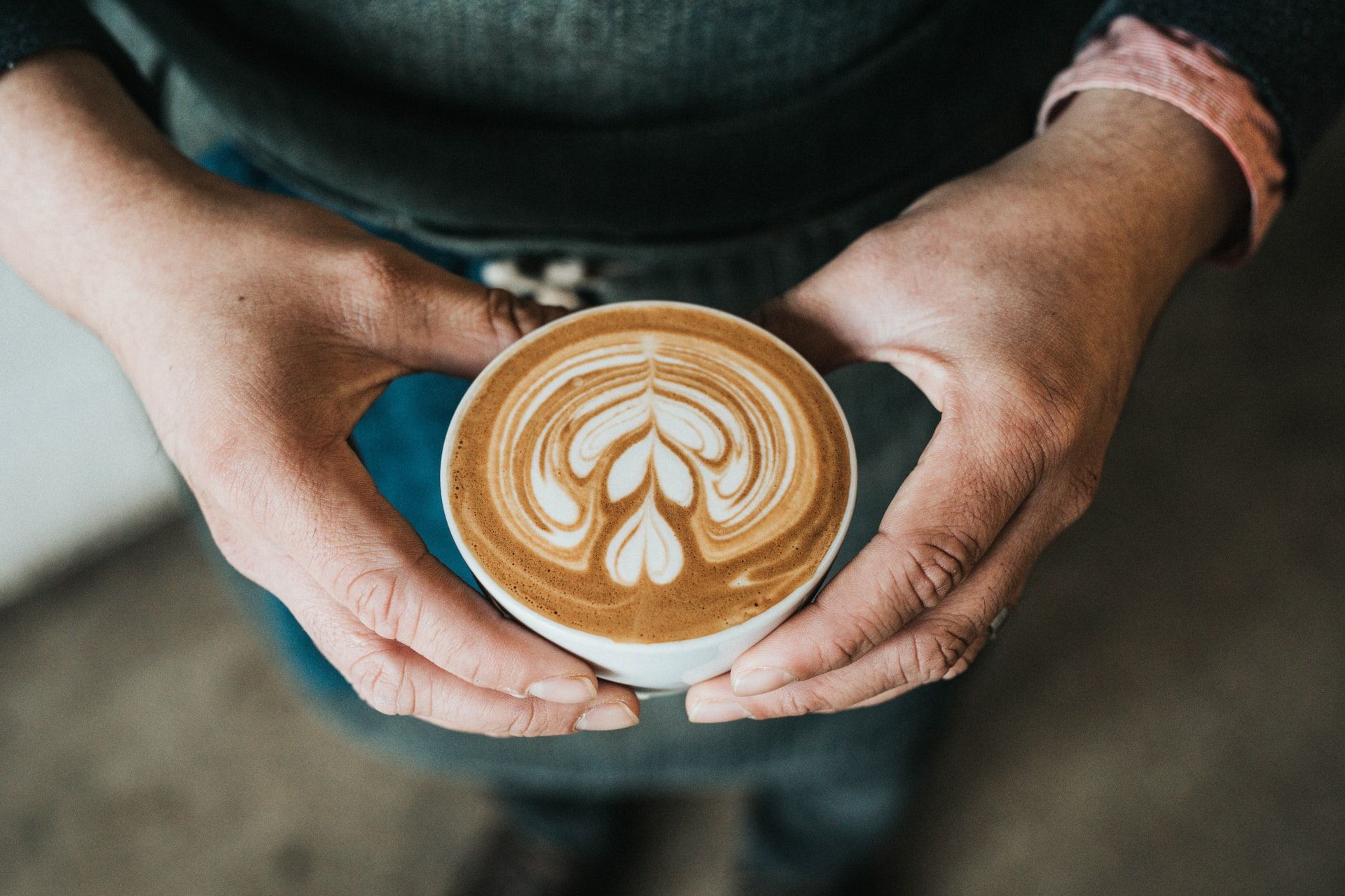 A person holding a flat white coffee with heart-shaped foam.