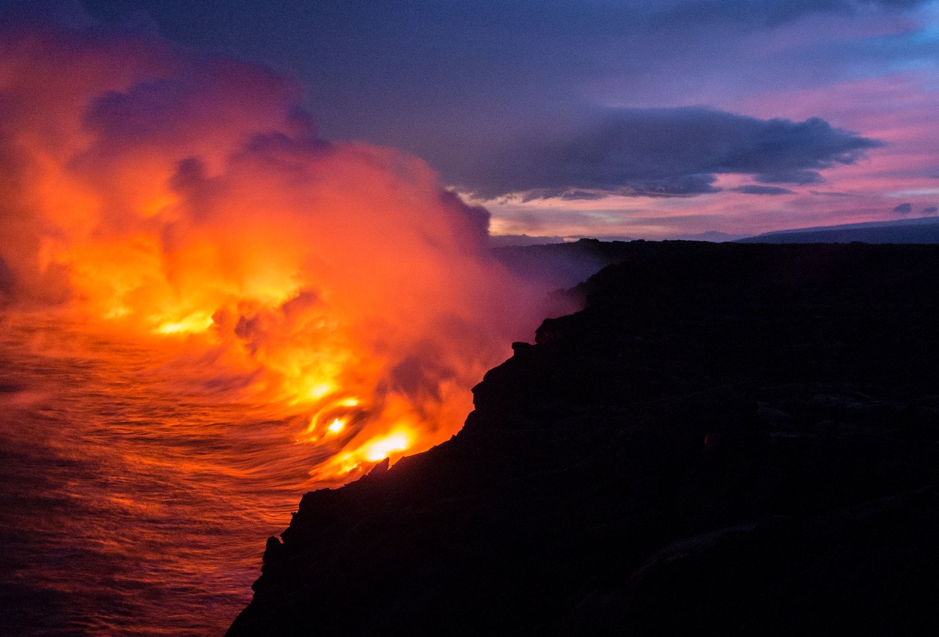 Lava fluindo de um vulcão para a água com nuvens de vapor