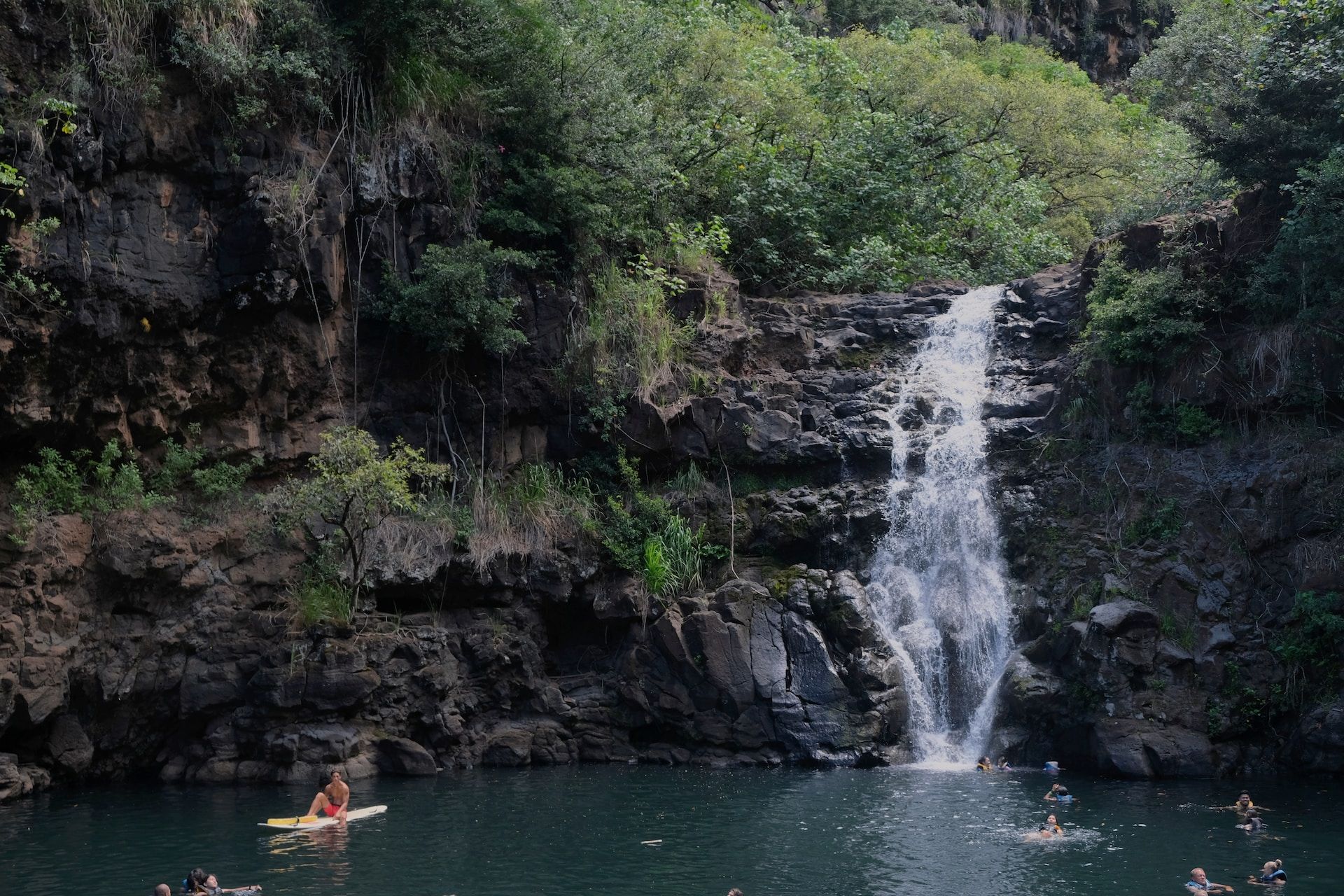 Lago entre um pequeno cânion com cachoeira e pessoas flutuando na água