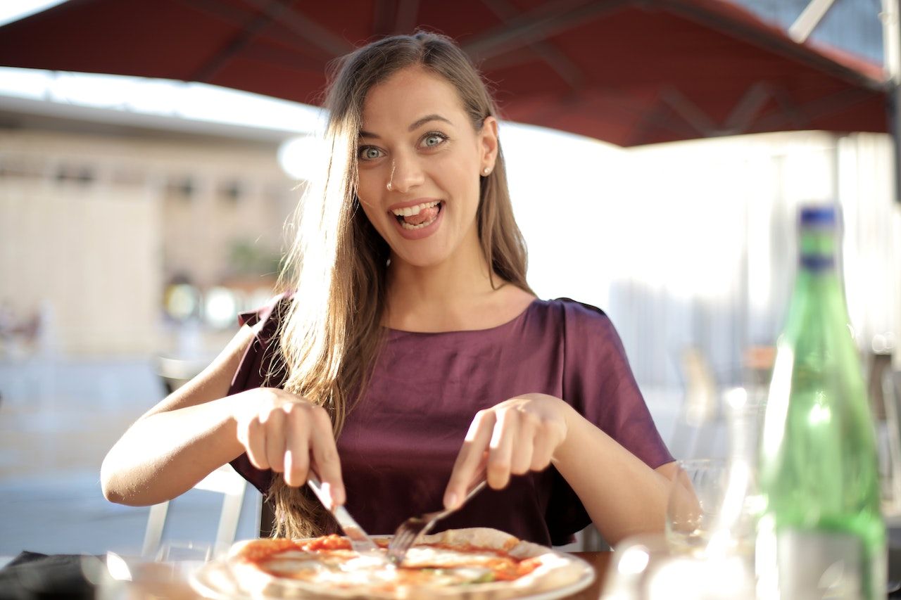 Uma mulher em top roxo cortando pizza