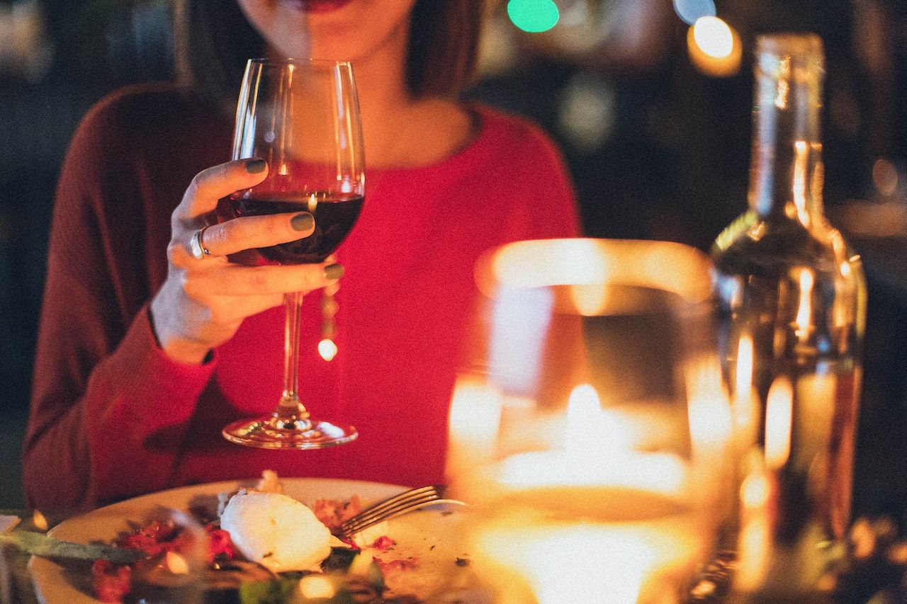Mulher de vermelho segurando uma taça de vinho com comida na mesa