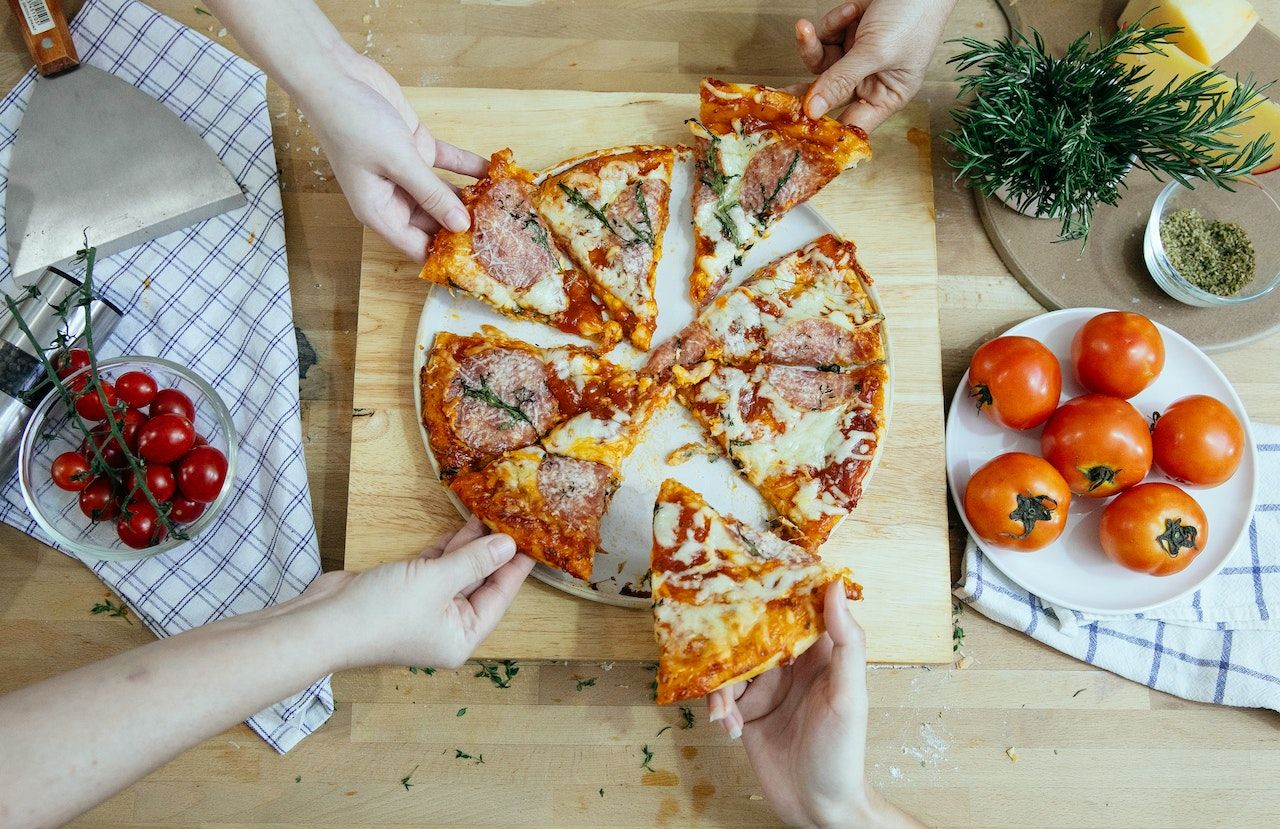 Pessoas compartilhando tamanhos de pizza na tábua de cortar