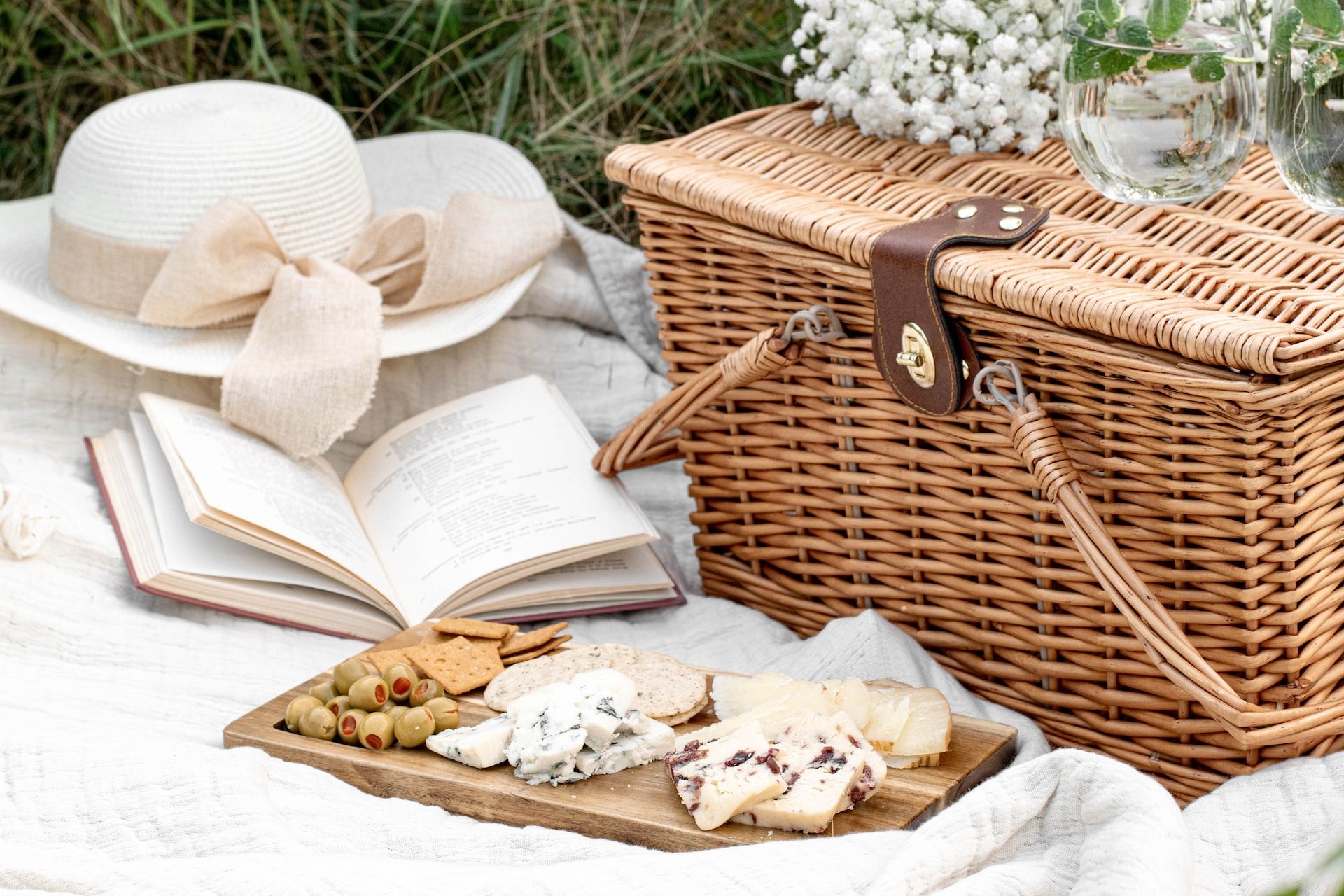 Picnic basket, white hat, and a book in a field during spring time