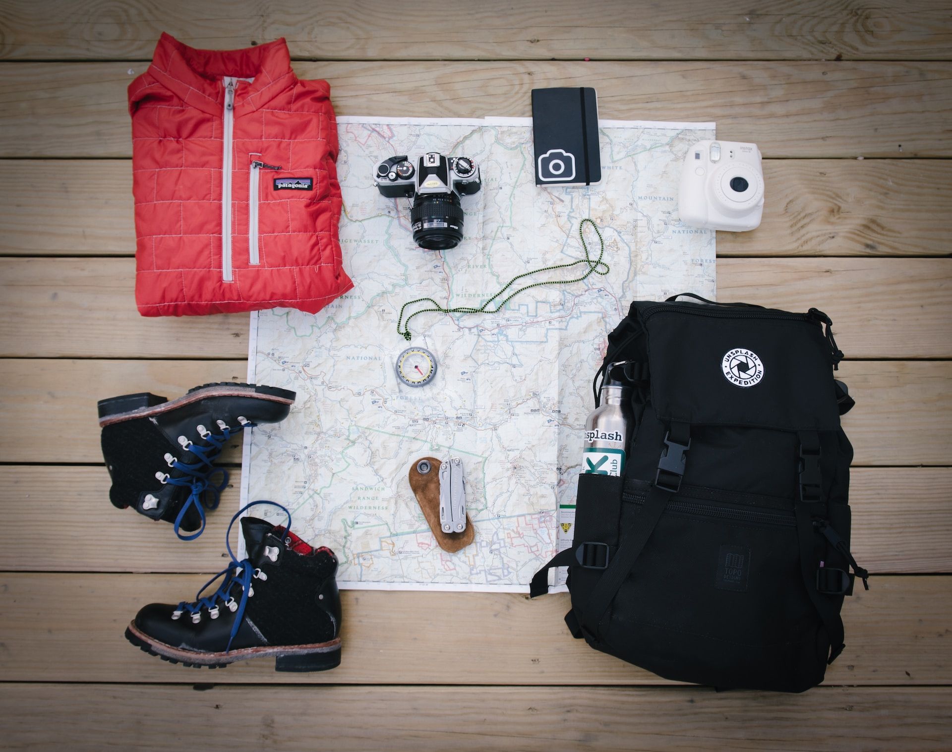 Packing for a hike: boots, a camera, a jacket, a compass, keys, and a backpack