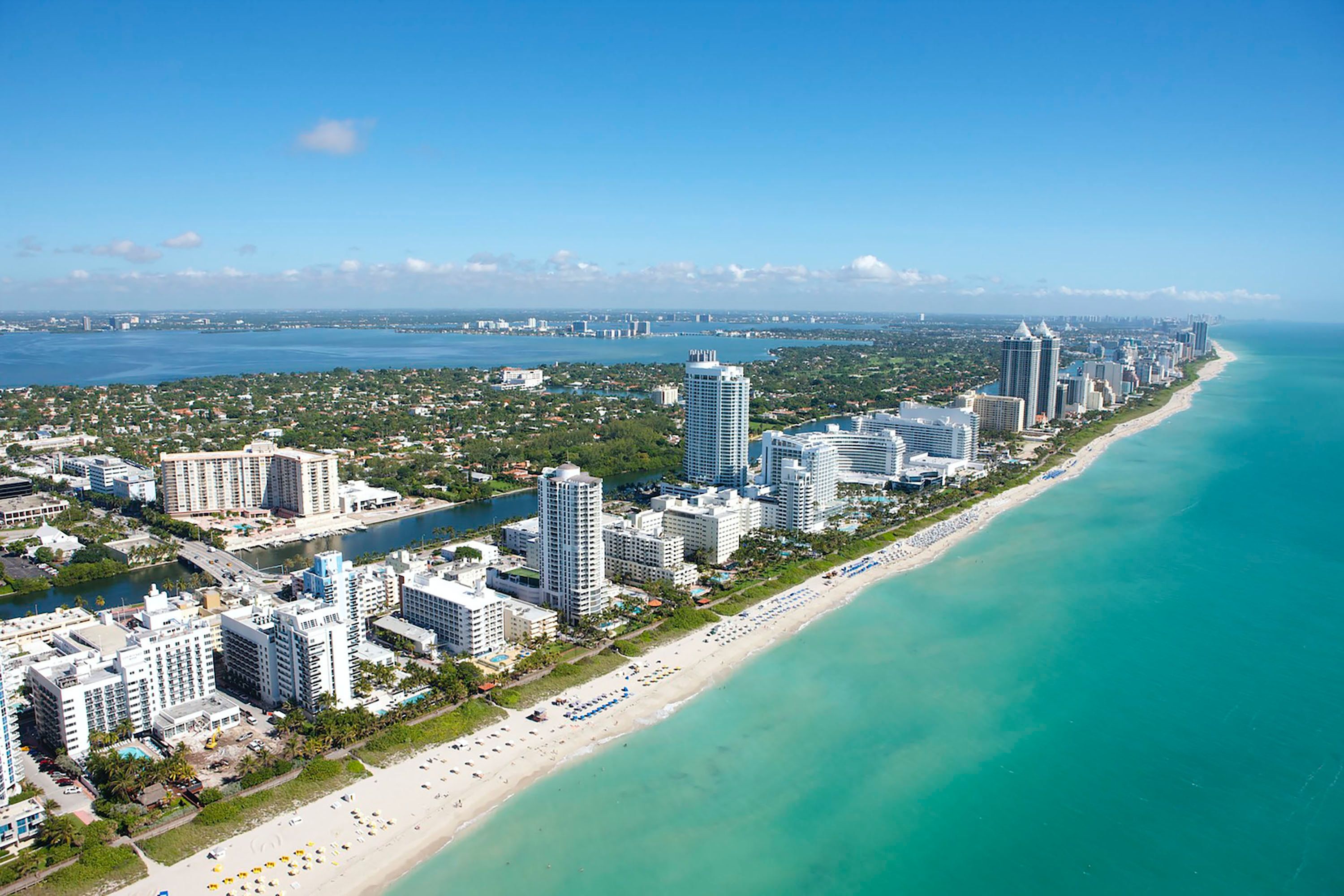 Blue waters and white sand beach with tall buildings on Miami Beach shore, Florida, USA