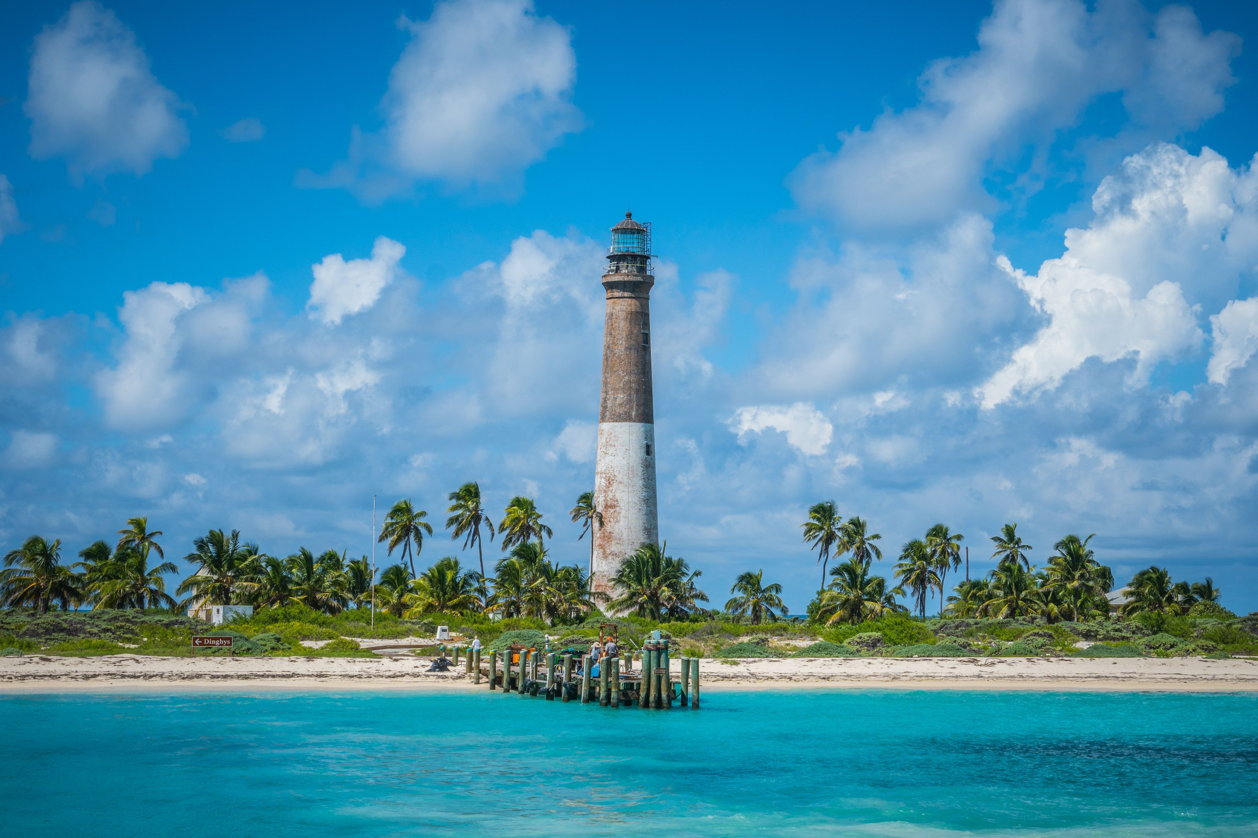 A white sandy shore separating a water body and an island with a lighthouse surrounded by trees in Dry Tortugas National Park