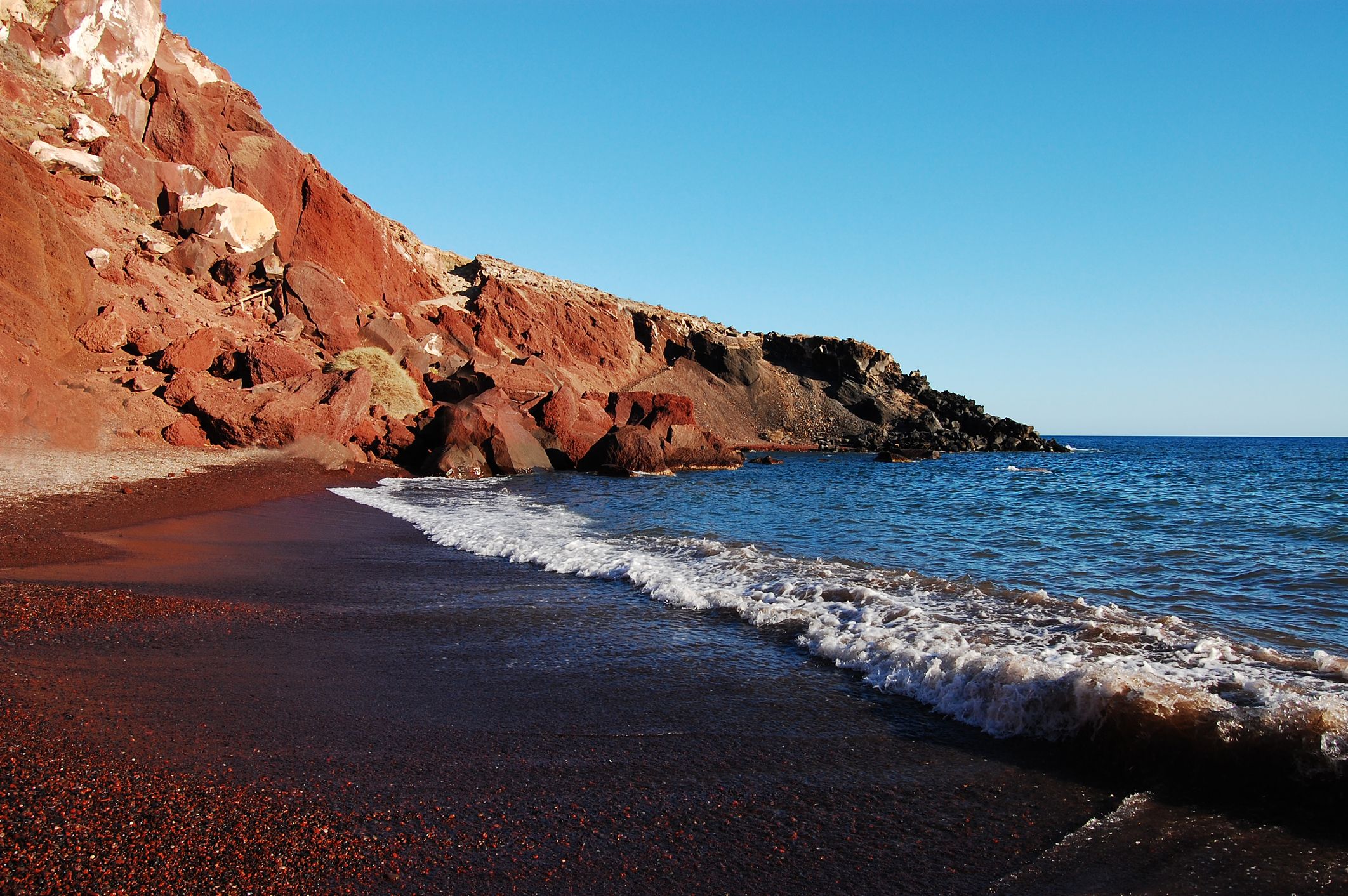 Κύματα που σκάνε στην κόκκινη παραλία με τους κόκκινους βραχώδεις βράχους