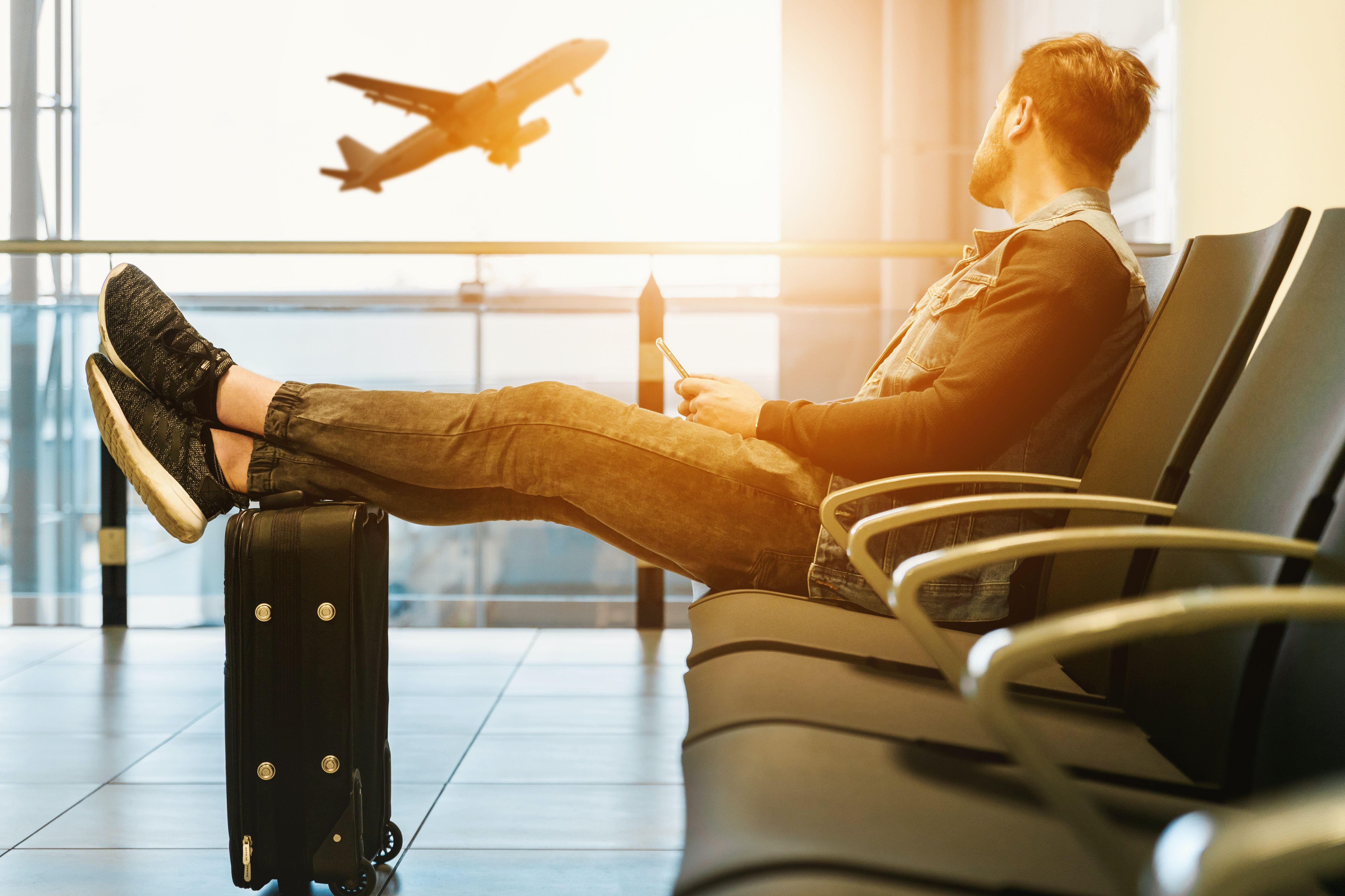 man sitting on a chair at the airport watching a plane 