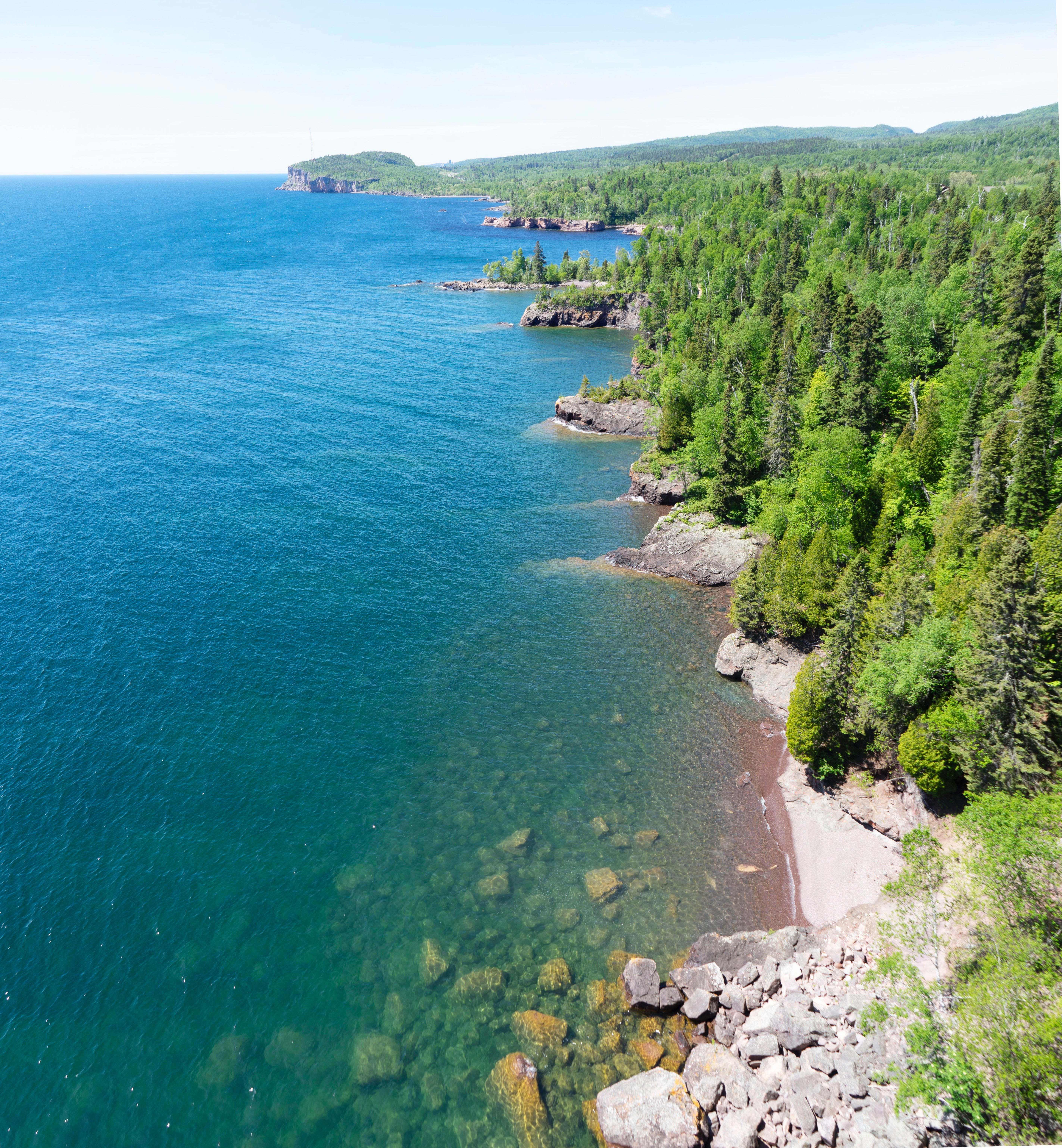 blue water and rocky shore line with forest 