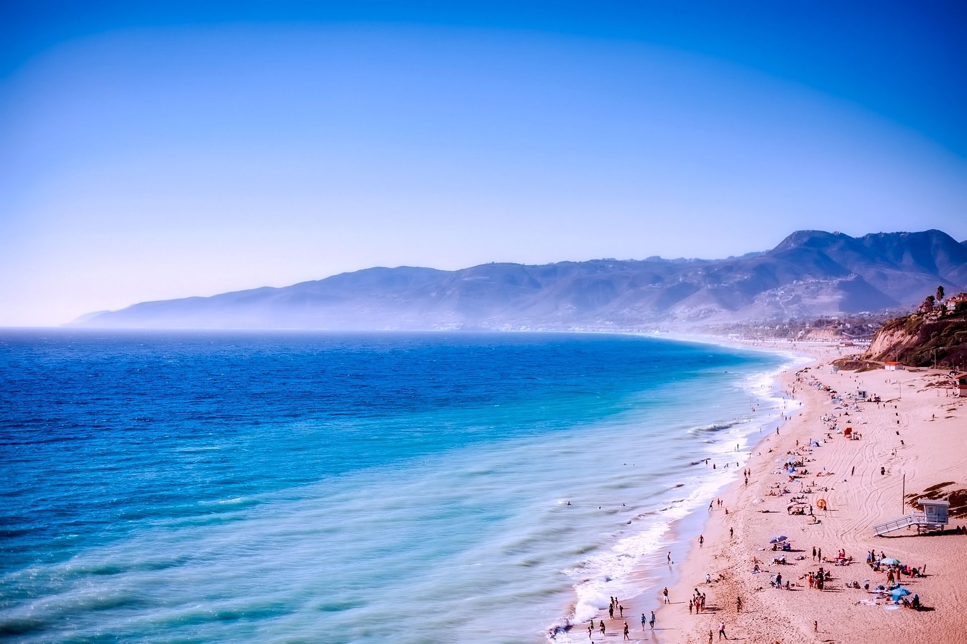 An aerial view of a sandy shore, a blue water body and a blue sky in Malibu