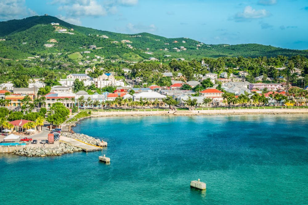 See the beach, houses, and green hills in Frederiksted, St.  Croix