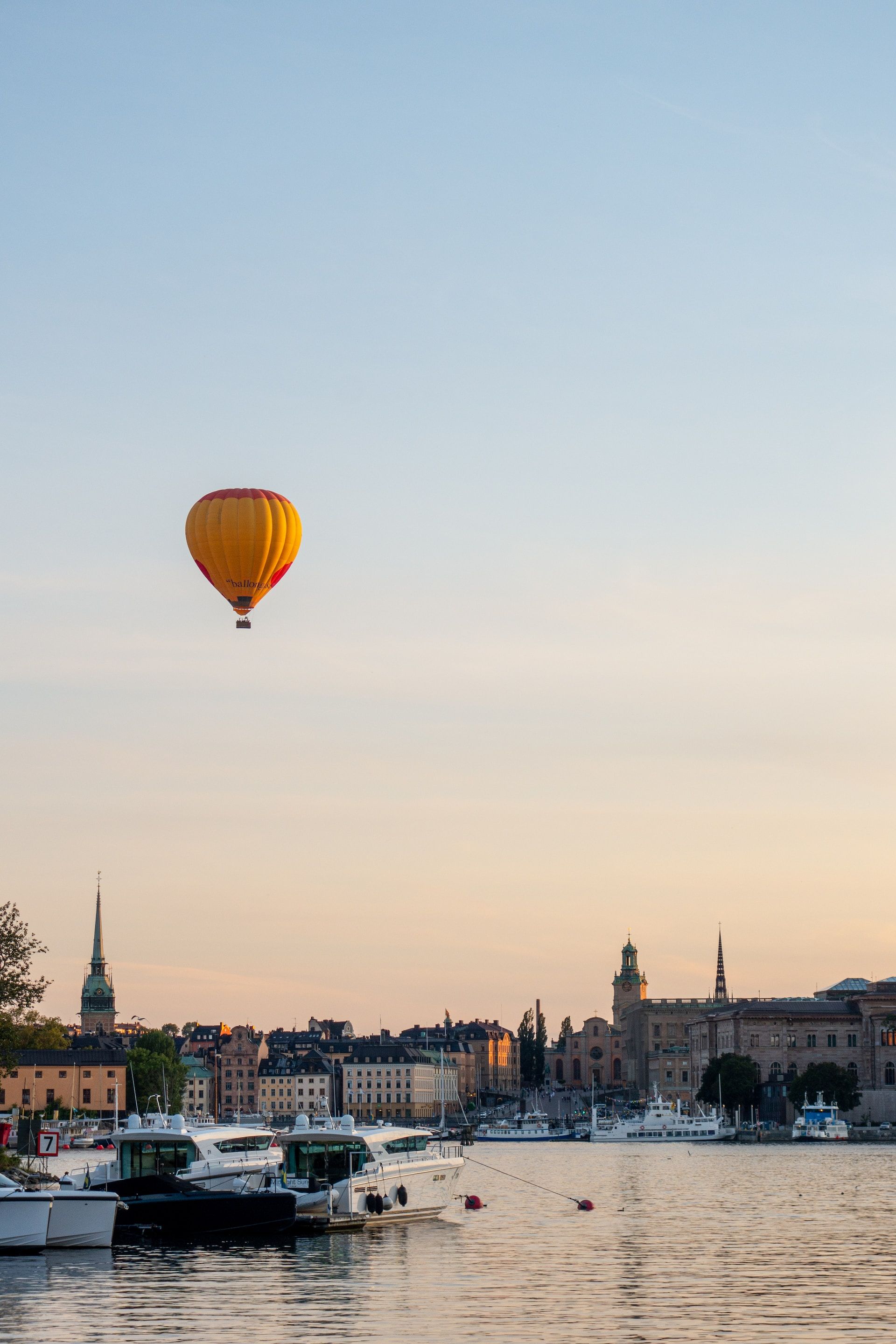 A hot air balloon floats above Stockholm during a vibrant, summer sunset.