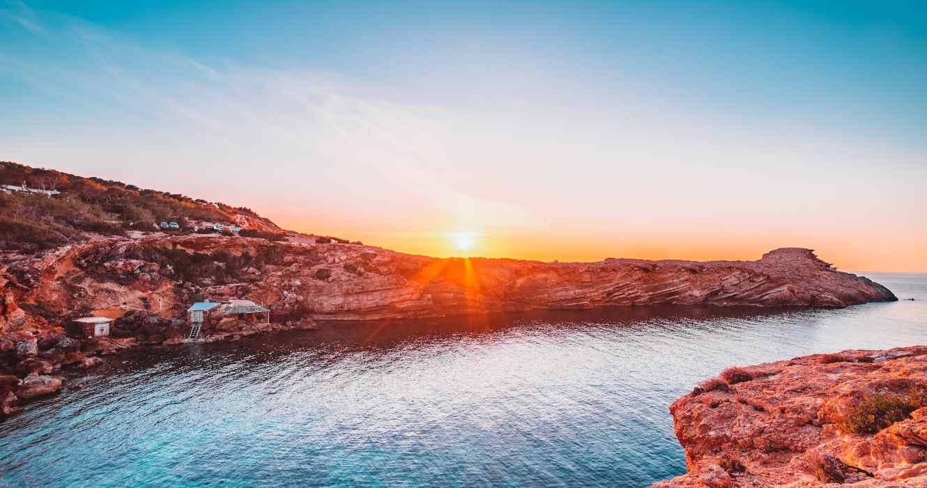 Sunset in a beach cove with traditional fishing huts and rock formations in Punta Galera, Ibiza