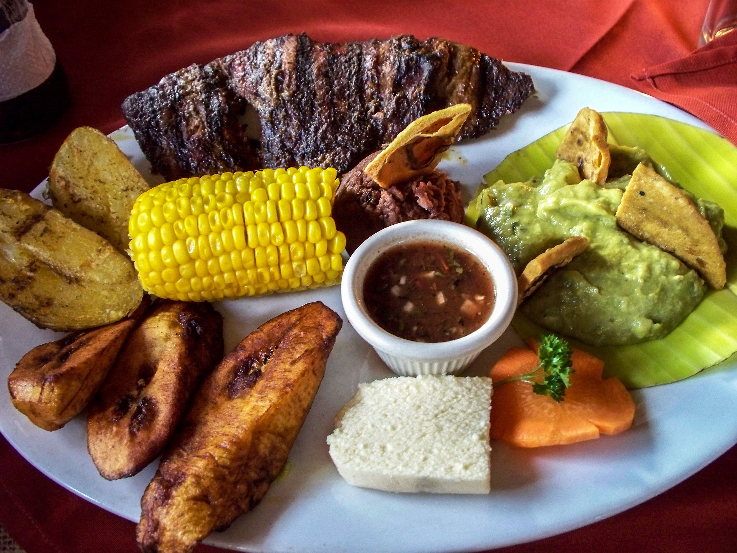 Plate of Guatemalan food: corn, potatoes, meat, plantains, avocado, carrot, bread.