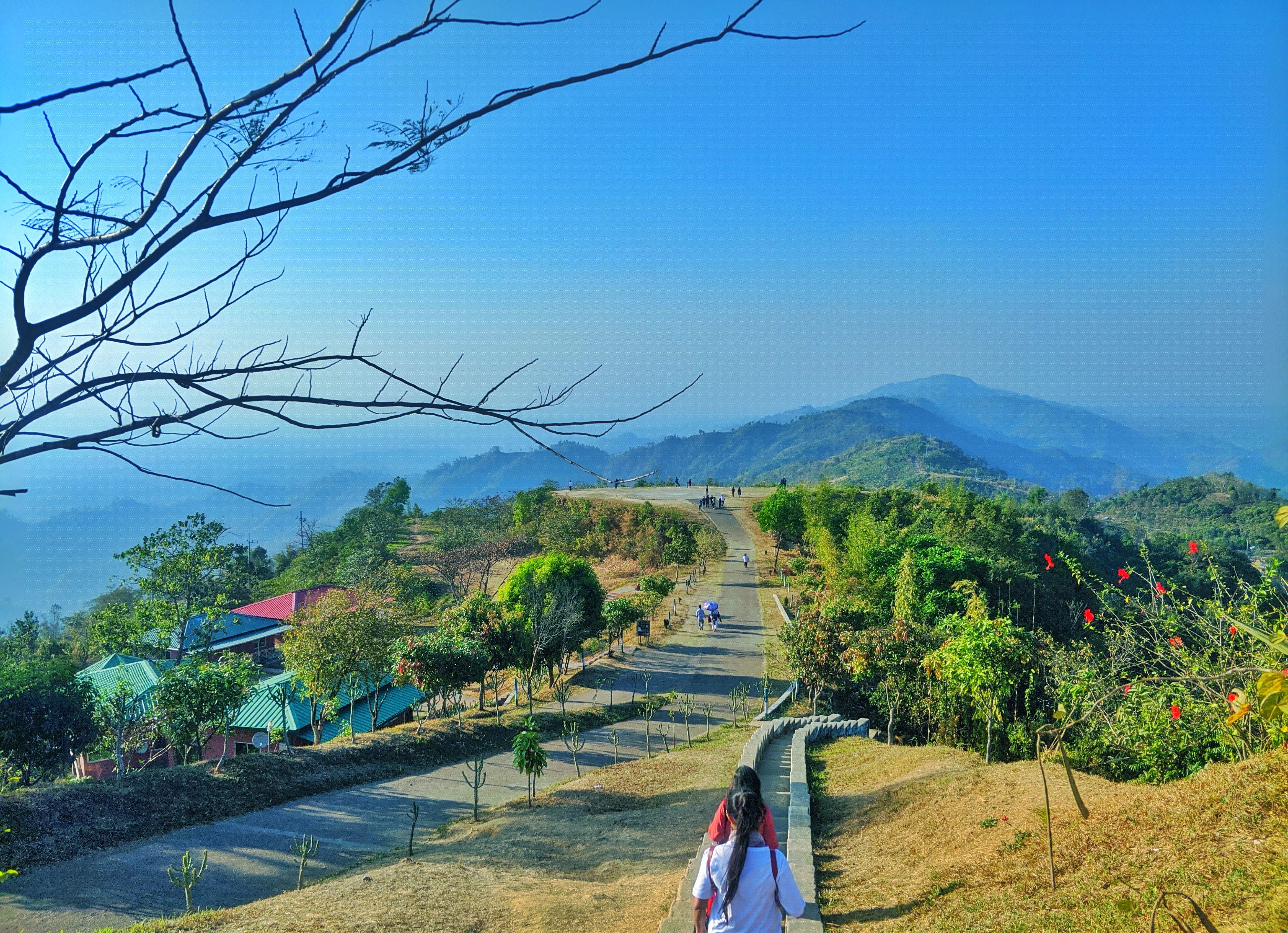 people walking on a path alongside a road in lush green mountains 